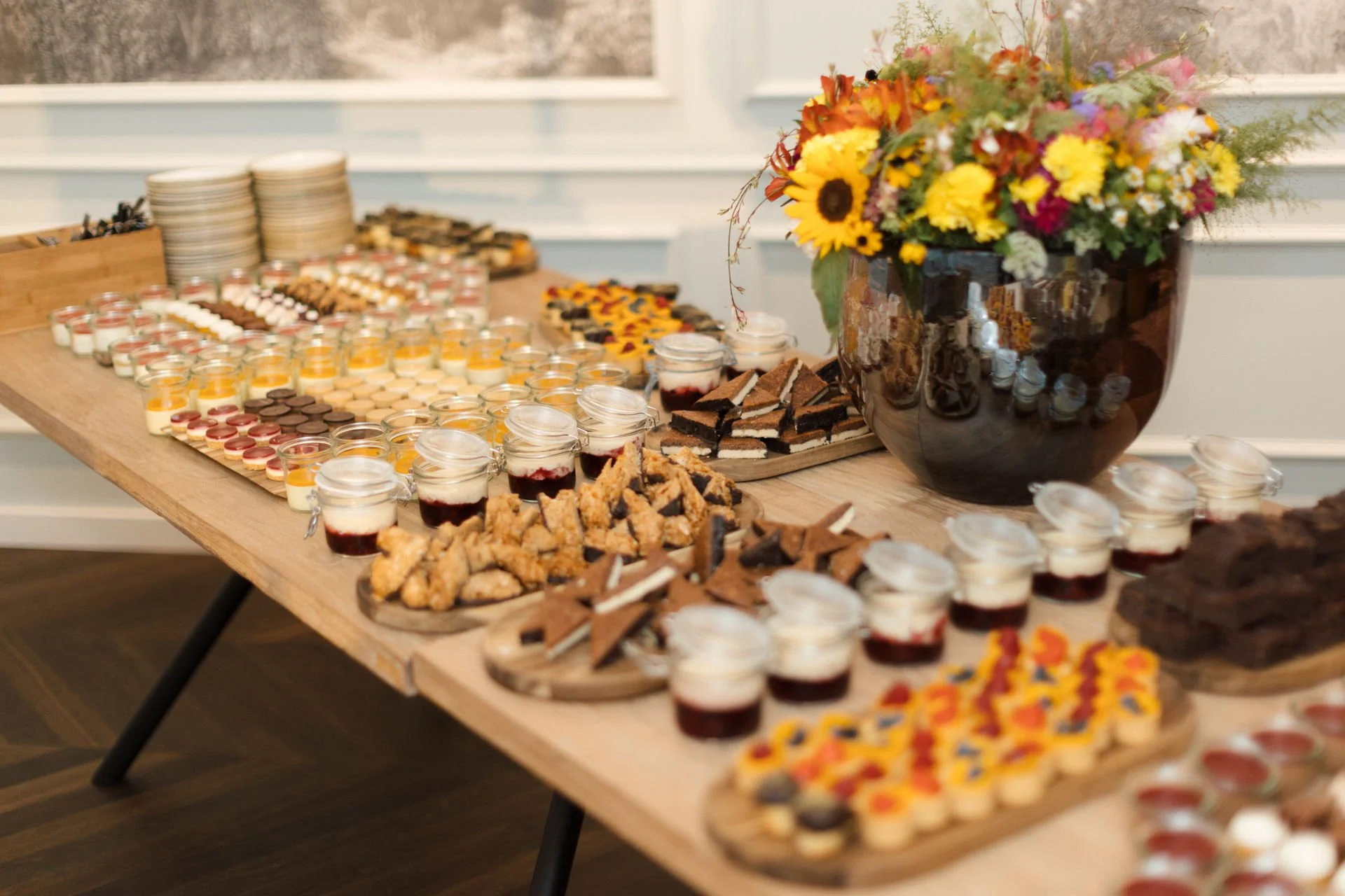 Buffet mit verschiedenen Desserts und eine große Vase mit bunten Blumen.