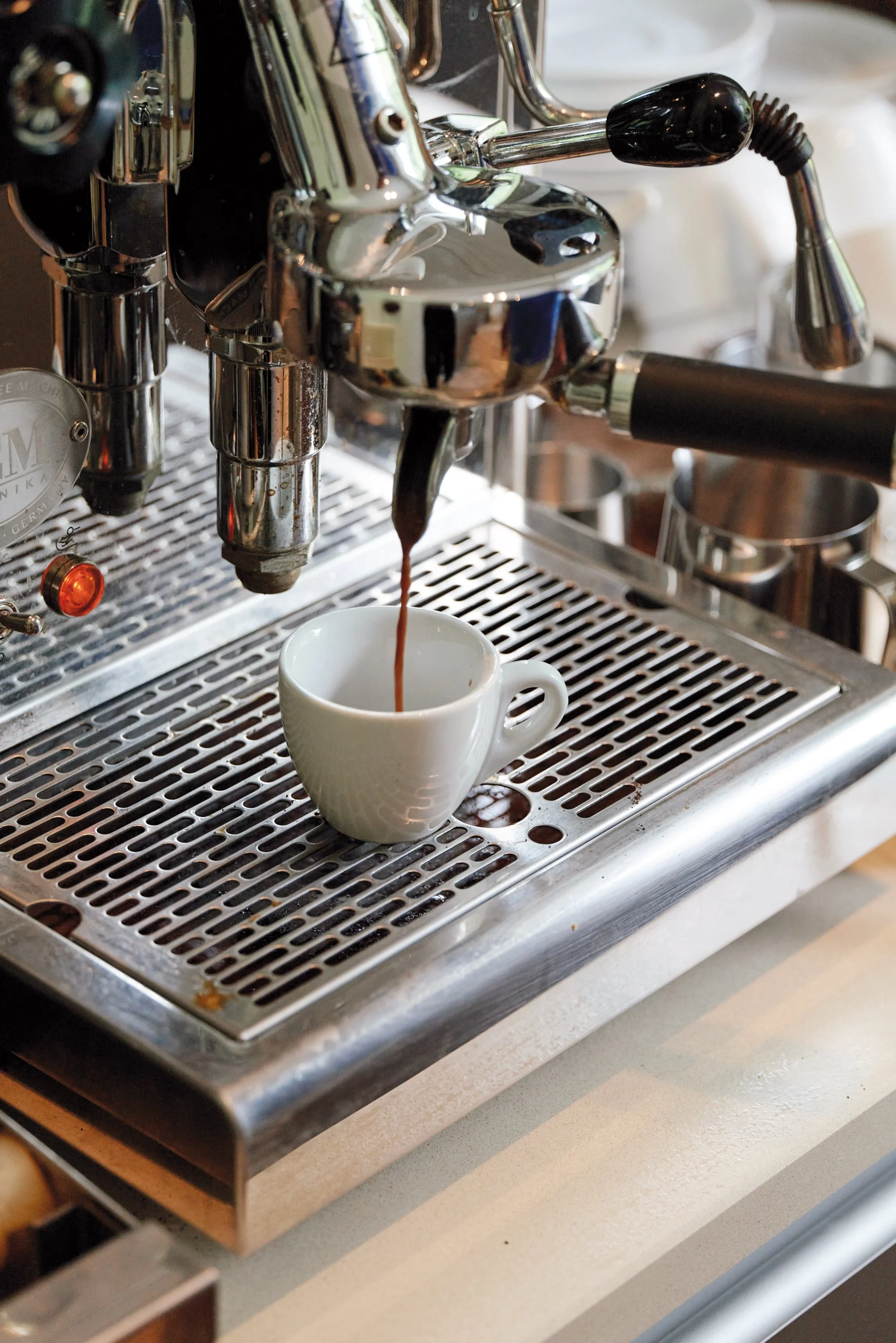 Eine Espressomaschine brüht einen Espresso in eine weiße Tasse auf einer Metallablage.