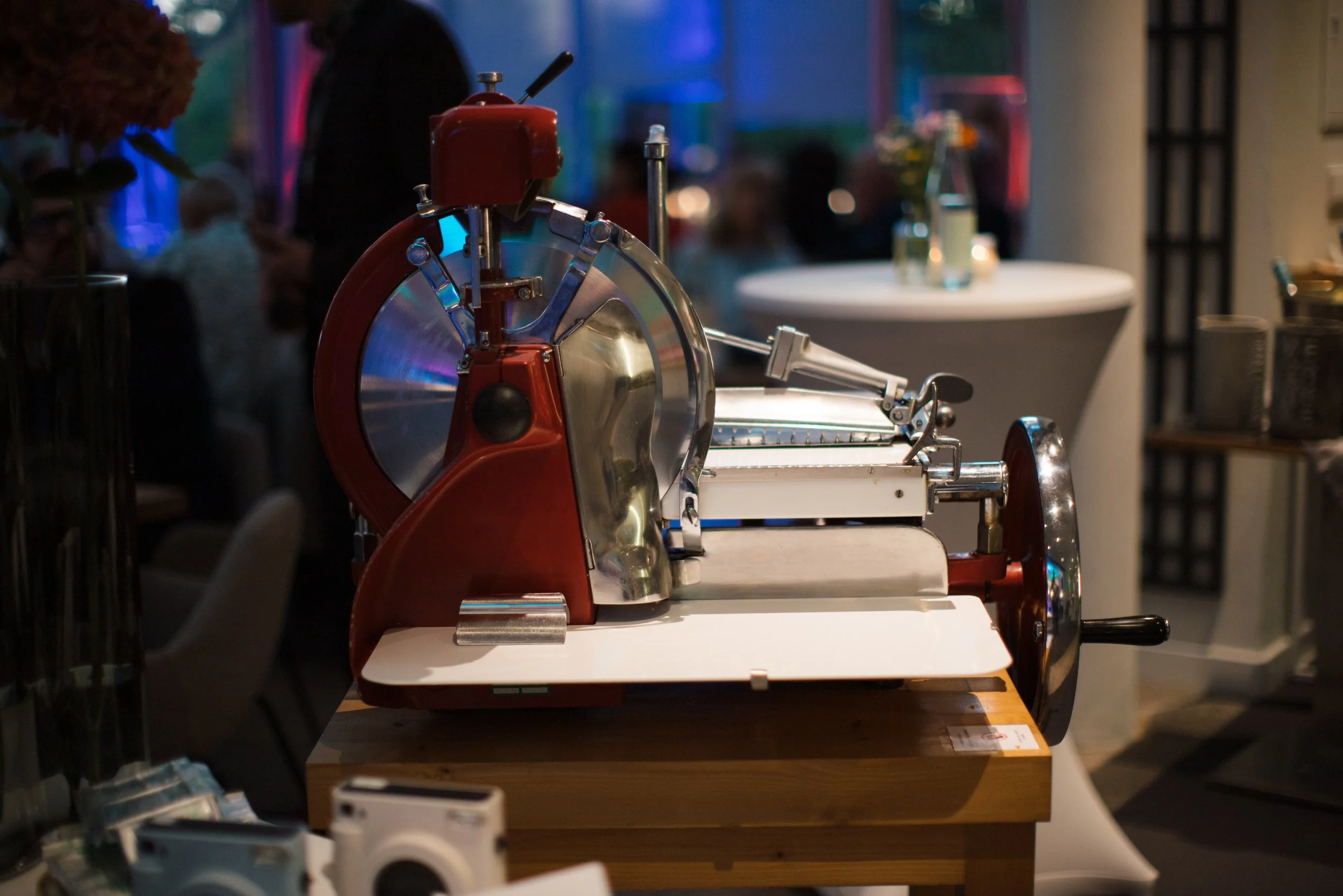 Historisches Fleischmetzgerät auf einem Holztisch bei einer Veranstaltung im Hintergrund mit Gästen und Dekoration.