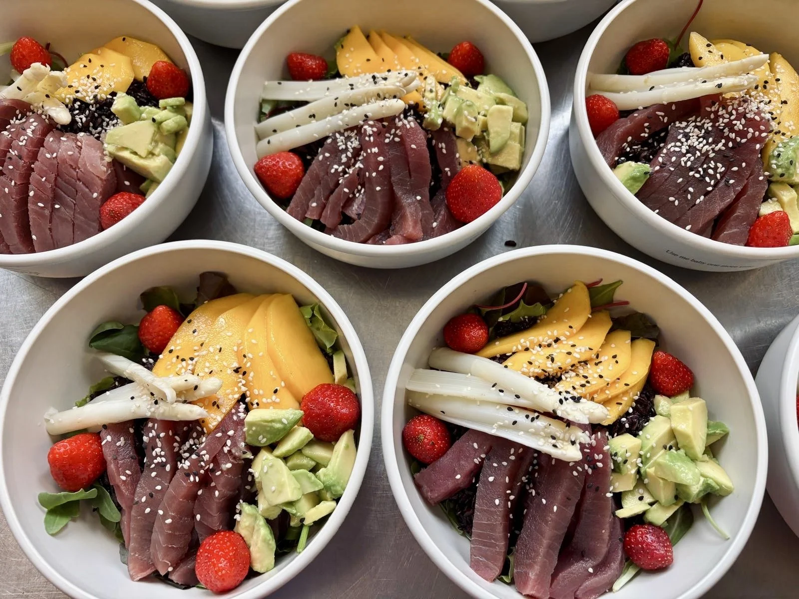 Schüsseln mit Salat, bestehend aus Thunfisch, Erdbeeren, Avocado, Mango, Zwiebel, Salat und Sesam.