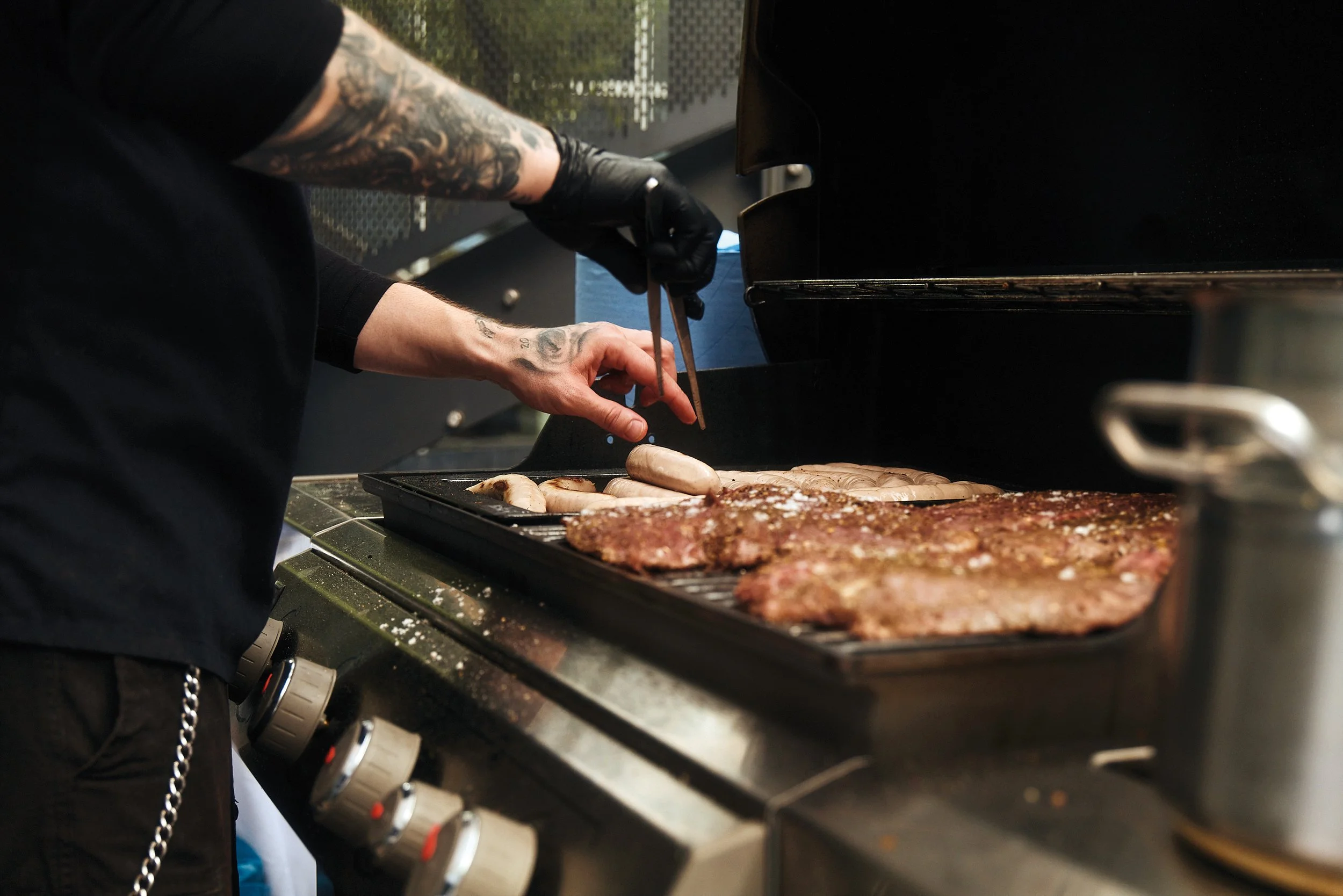 Ein Koch bereitet Grillfleisch und Würstchen auf einem Grill vor.