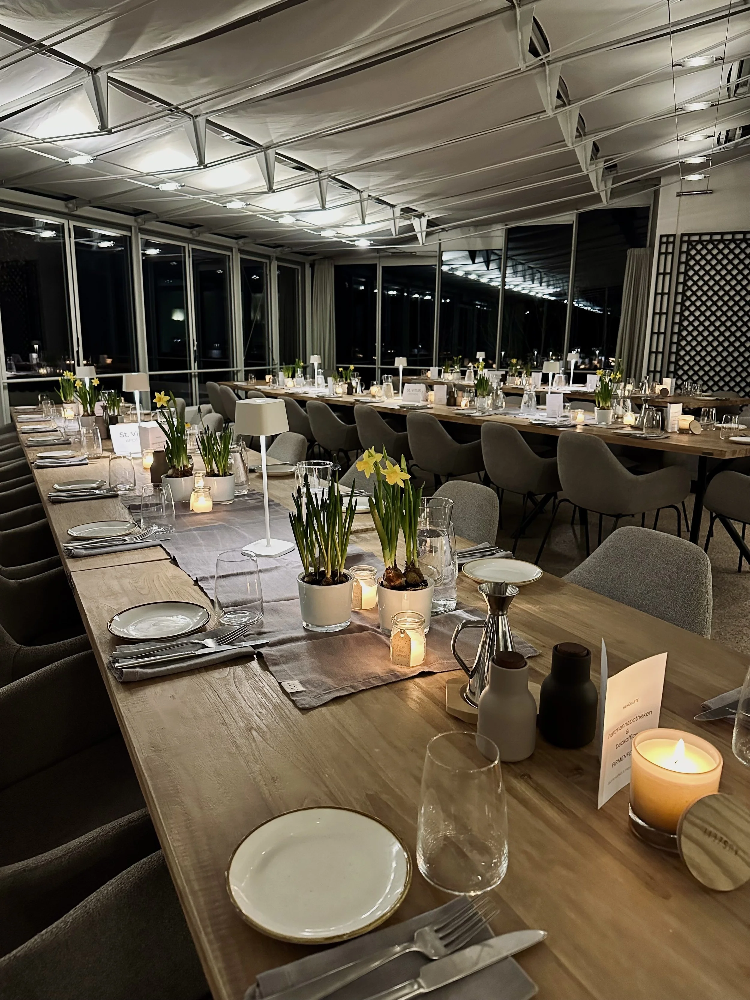 Elegant gedeckte Tafel in einem festlichen Raum mit Kerzen, Blumen und Platzkarten.