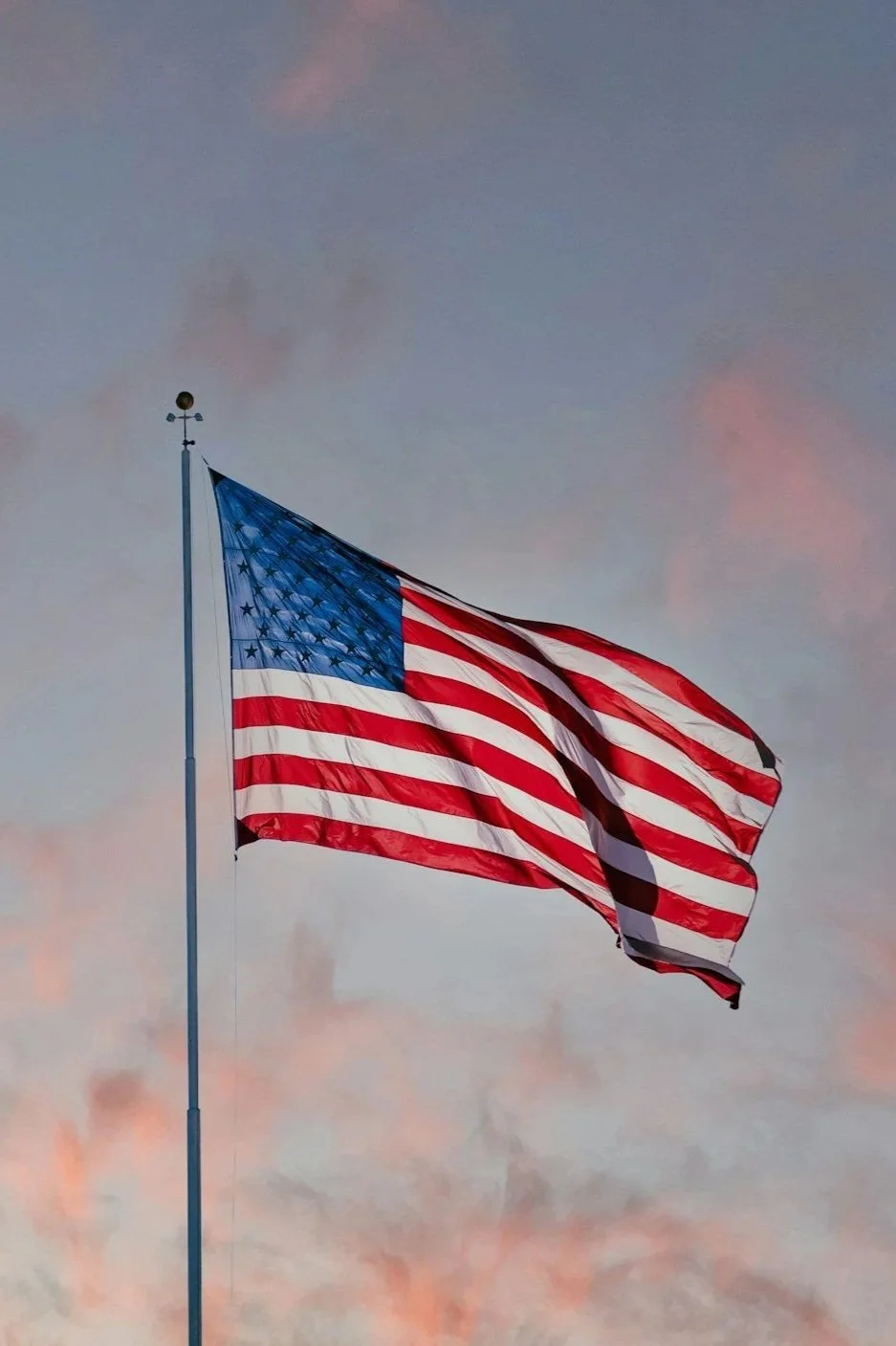 American flag flying in the wind against a cloudy sky at sunset.