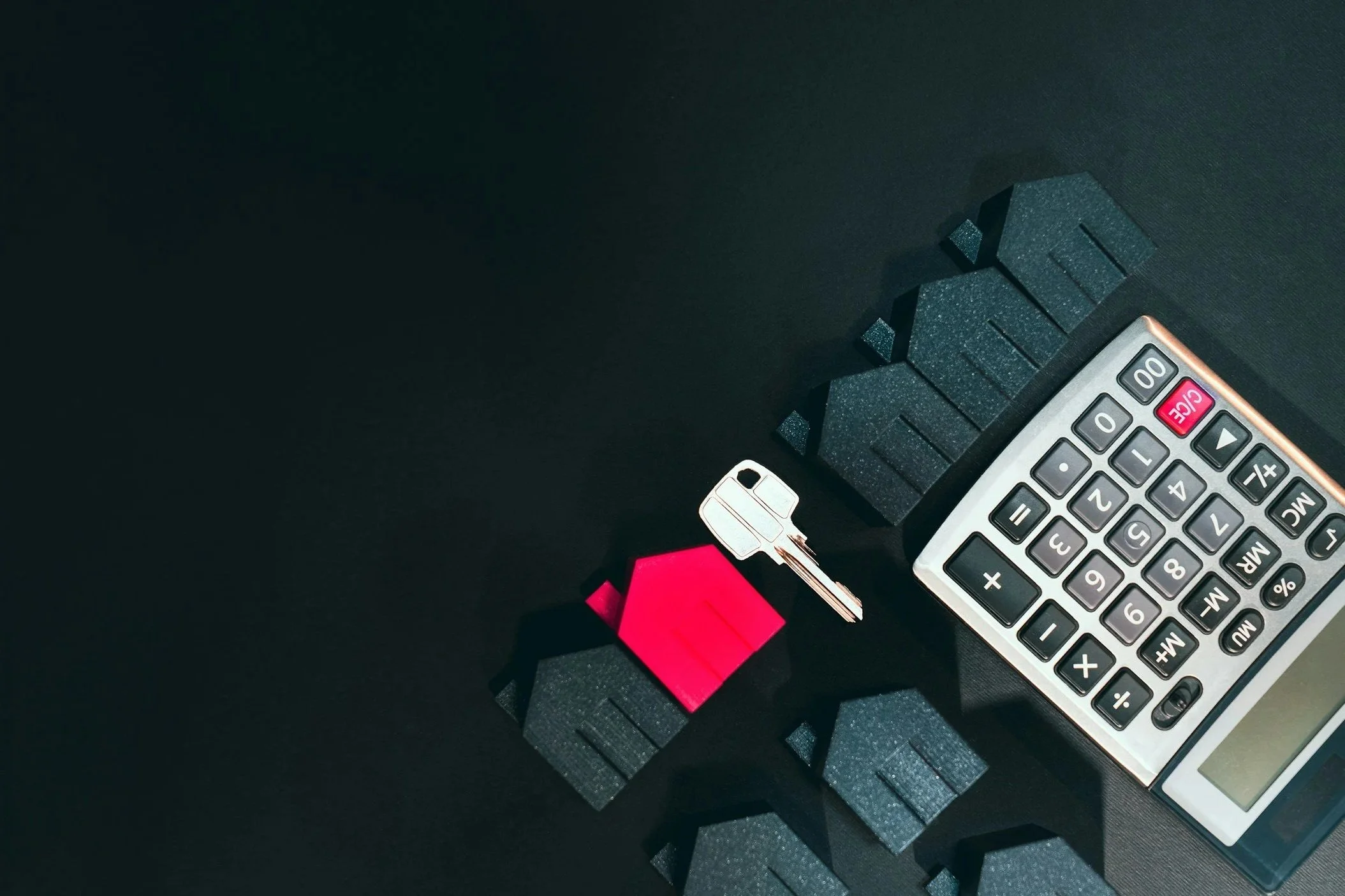 A set of small black building blocks, a key with a pink keychain, a red sticky note, and a calculator on a dark surface.