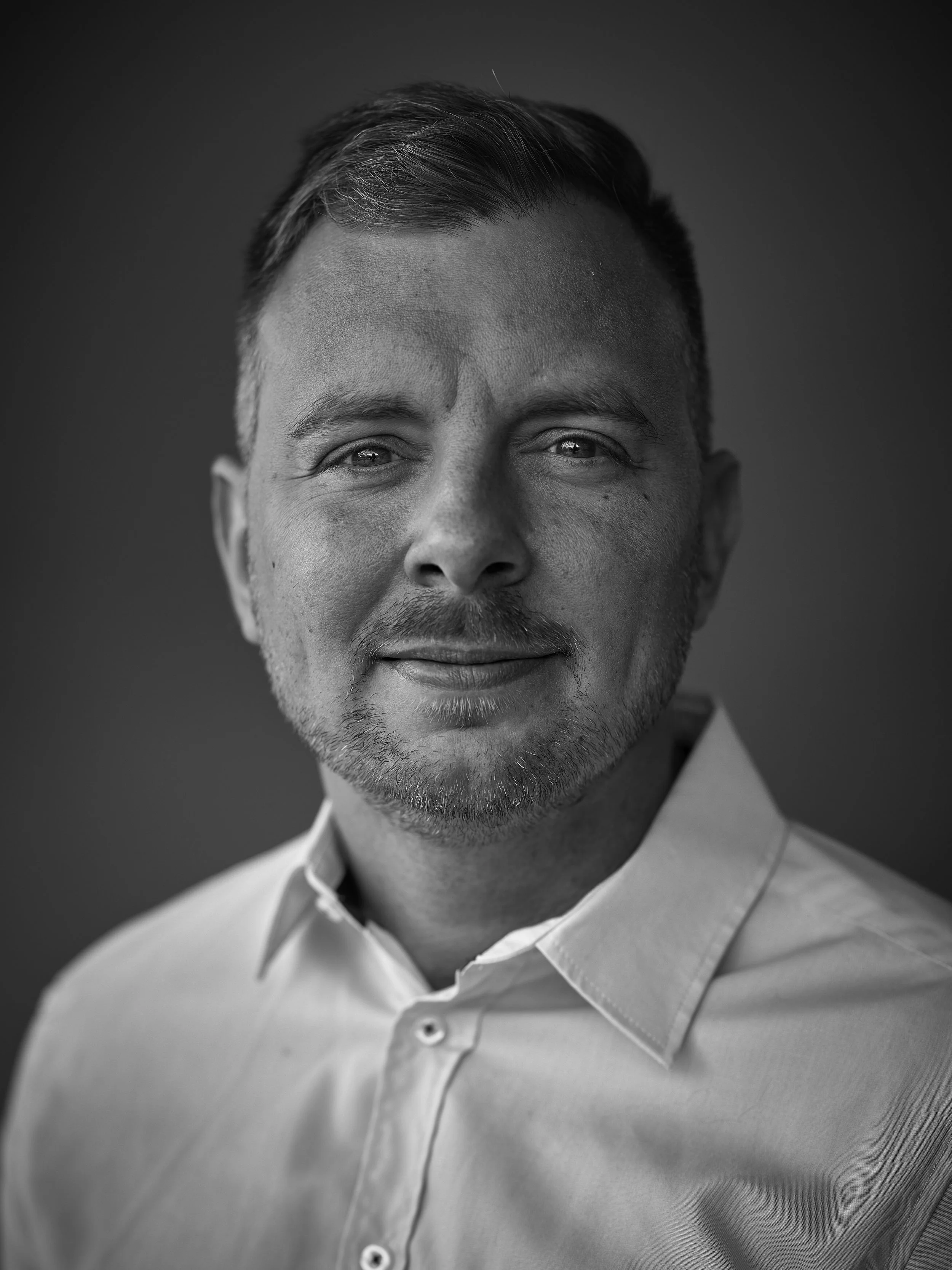 A black and white close-up portrait of a smiling man wearing a collared shirt.