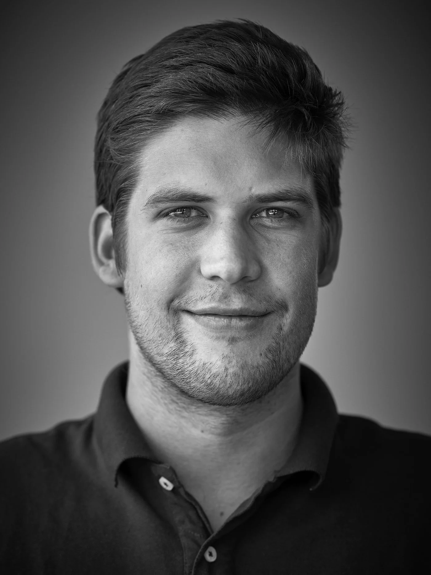 Black and white portrait of a young man with short, styled hair, smiling softly, wearing a dark collared shirt.