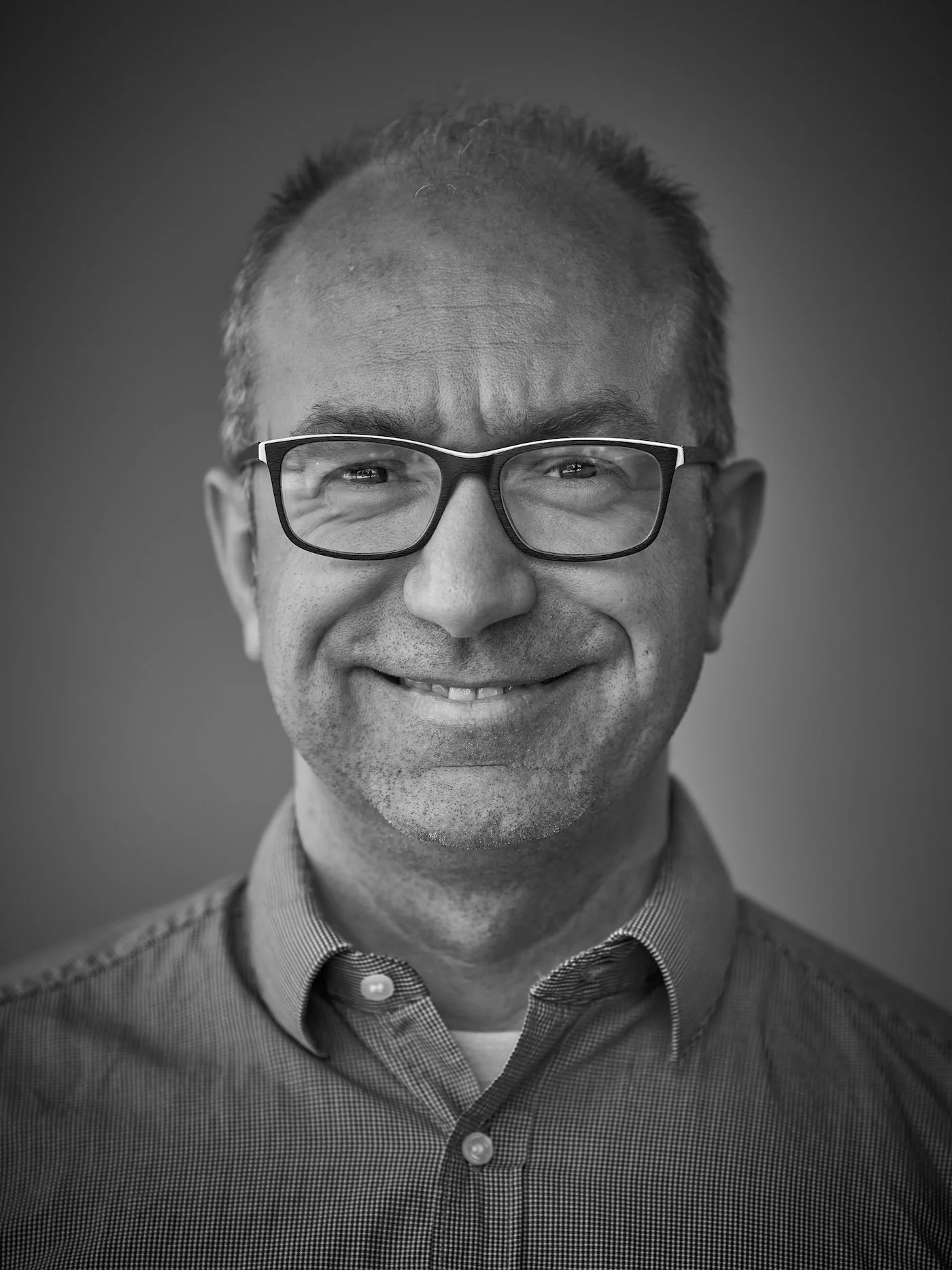Black and white portrait of a man wearing glasses and a collared shirt, smiling.