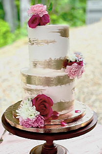 A three-tiered wedding cake decorated with pink and white flowers and gold accents.