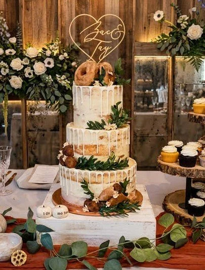 Three-tiered wedding cake with white icing, decorated with greenery and small donuts on top.