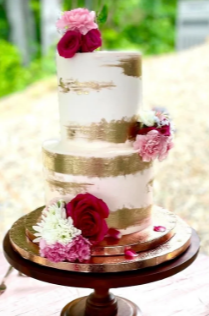 A three-tiered wedding cake decorated with pink and white flowers and gold accents.