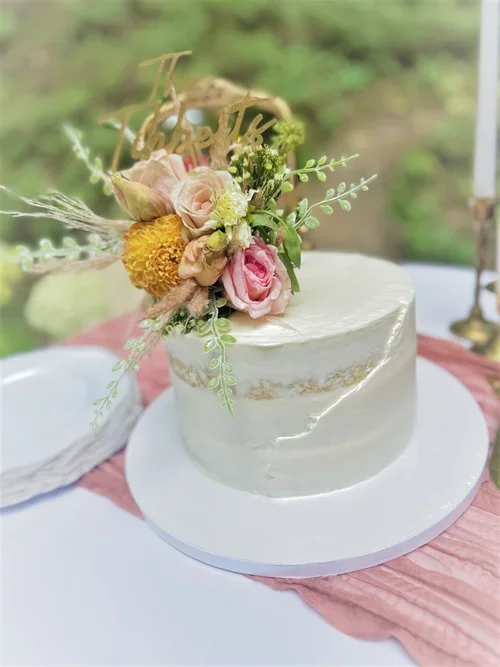 A white semi-naked cake with a floral arrangement on top.