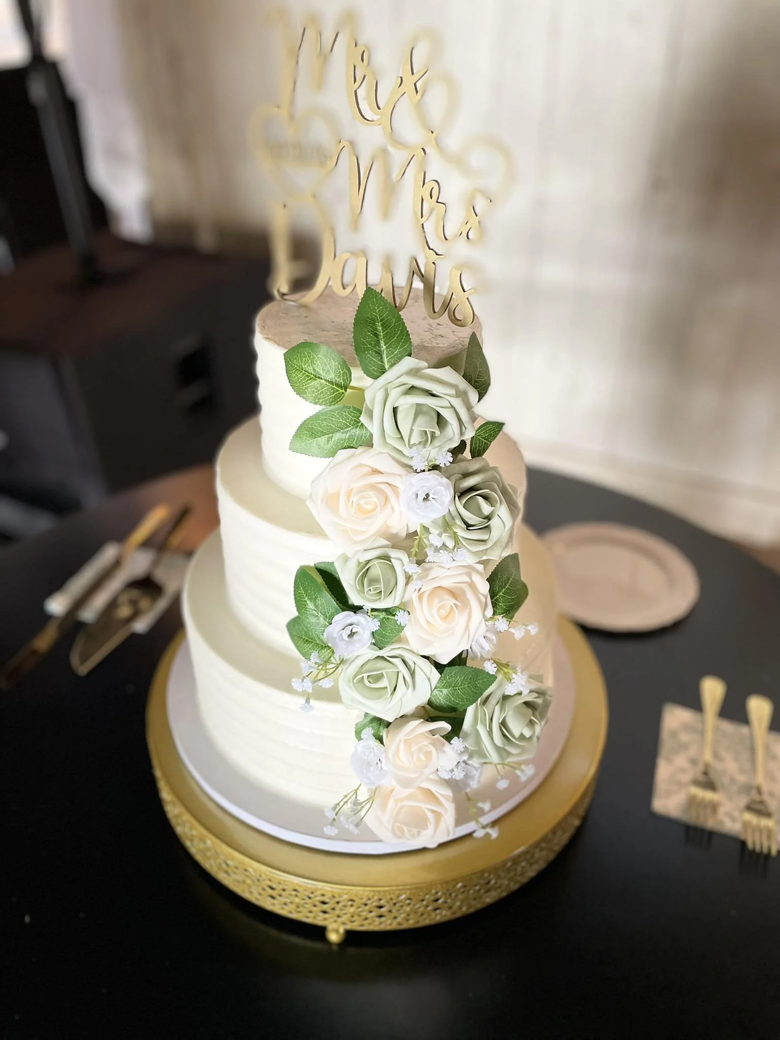A three-tier wedding cake decorated with white and light cream roses and greenery.