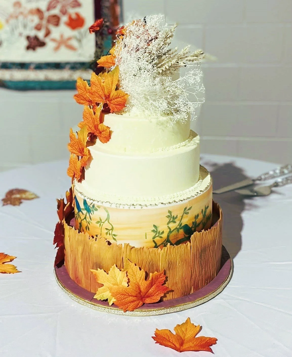 Four-tiered wedding cake decorated with fall leaves and white coral-like toppings and scattered leaves.