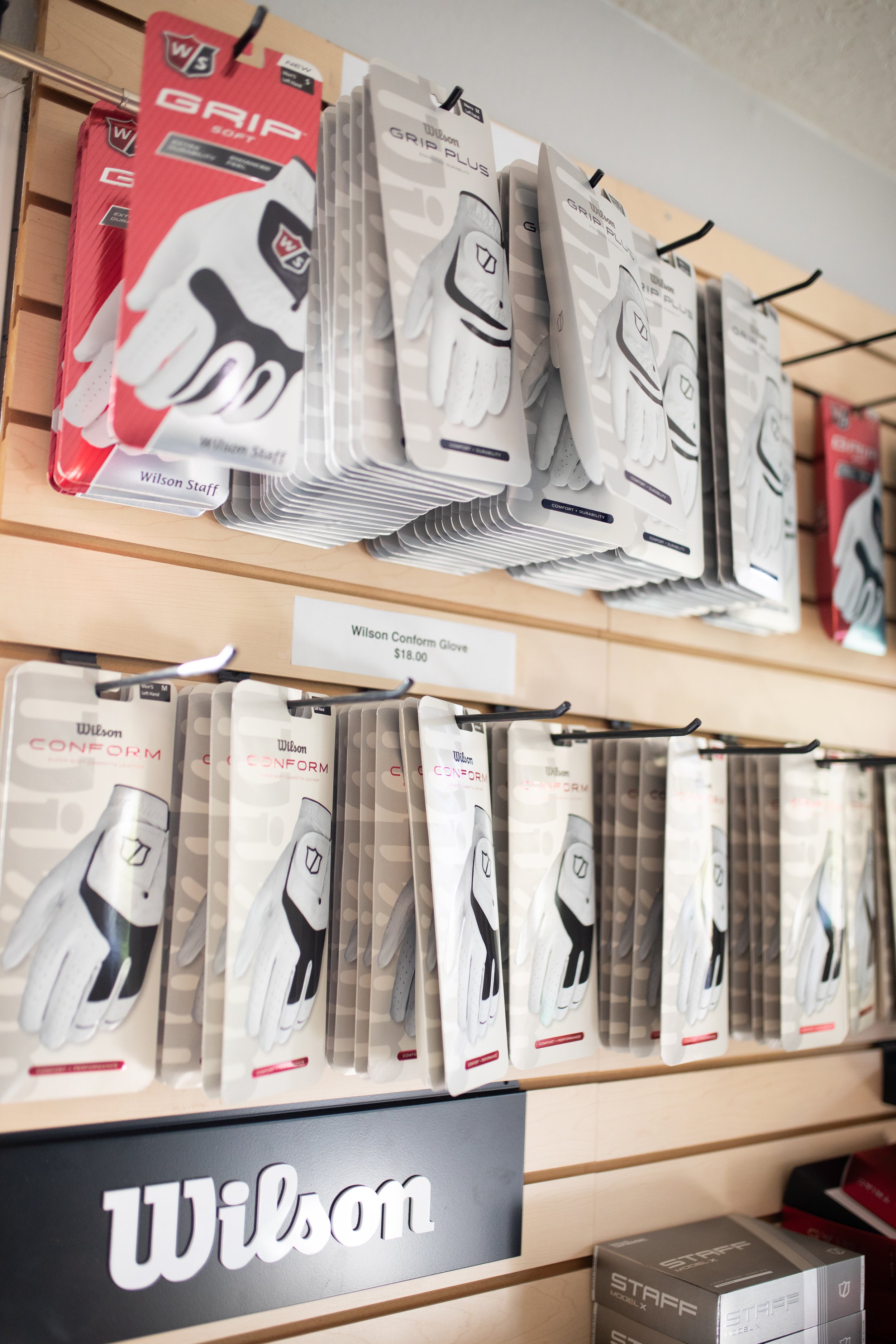 Display of Wilson golf gloves in red, white, and gray packaging on a store shelf.