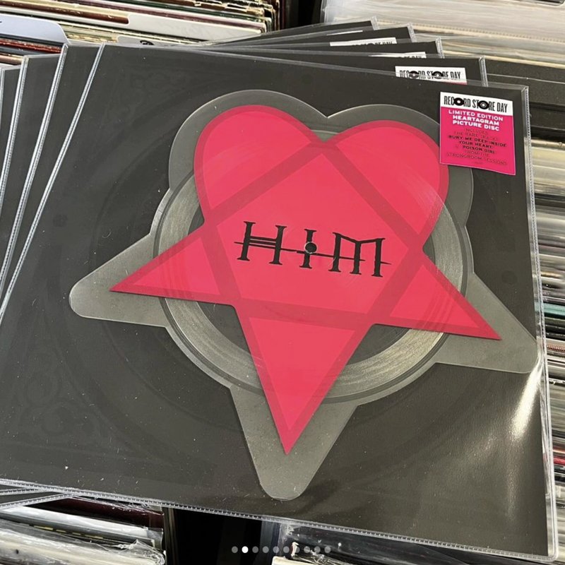 A vinyl record with a pink heart-shaped sticker in the center and the words "HIM" written in black, displayed among other records at a store.
