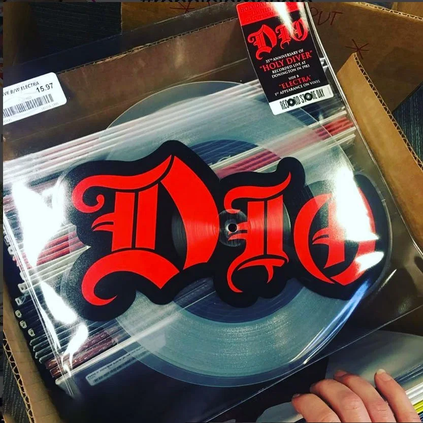 A vinyl record with a label that has the word 'Dio' in red Gothic font. The record is inside a clear plastic sleeve, with a sticker that mentions a 35th anniversary of 'Holy Diver' by Dio.