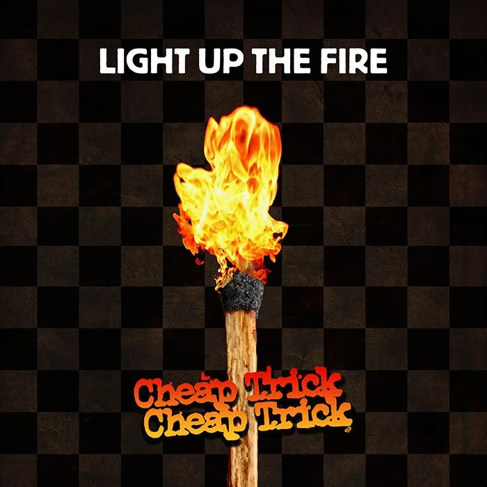 A matchstick with a flame on top, on a black checkered background. The text at the top says 'LIGHT UP THE FIRE'. Below the matchstick, there are two lines of text, 'Cheap Trick' in red and 'Cheap Trick' in yellow, stylized in a playful font.