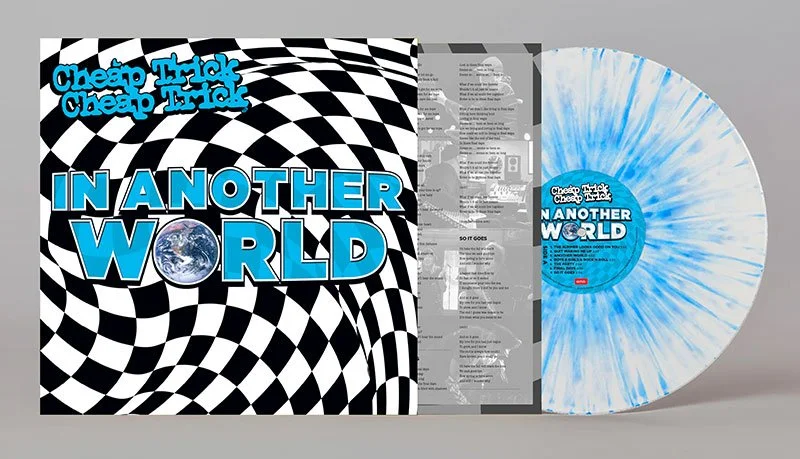 Vinyl record titled "In Another World" with a tie-dye blue and white splatter pattern, accompanied by album cover and lyrics insert for a band named "Cheap Trick" or "Cheap Trick Cheap Trick".