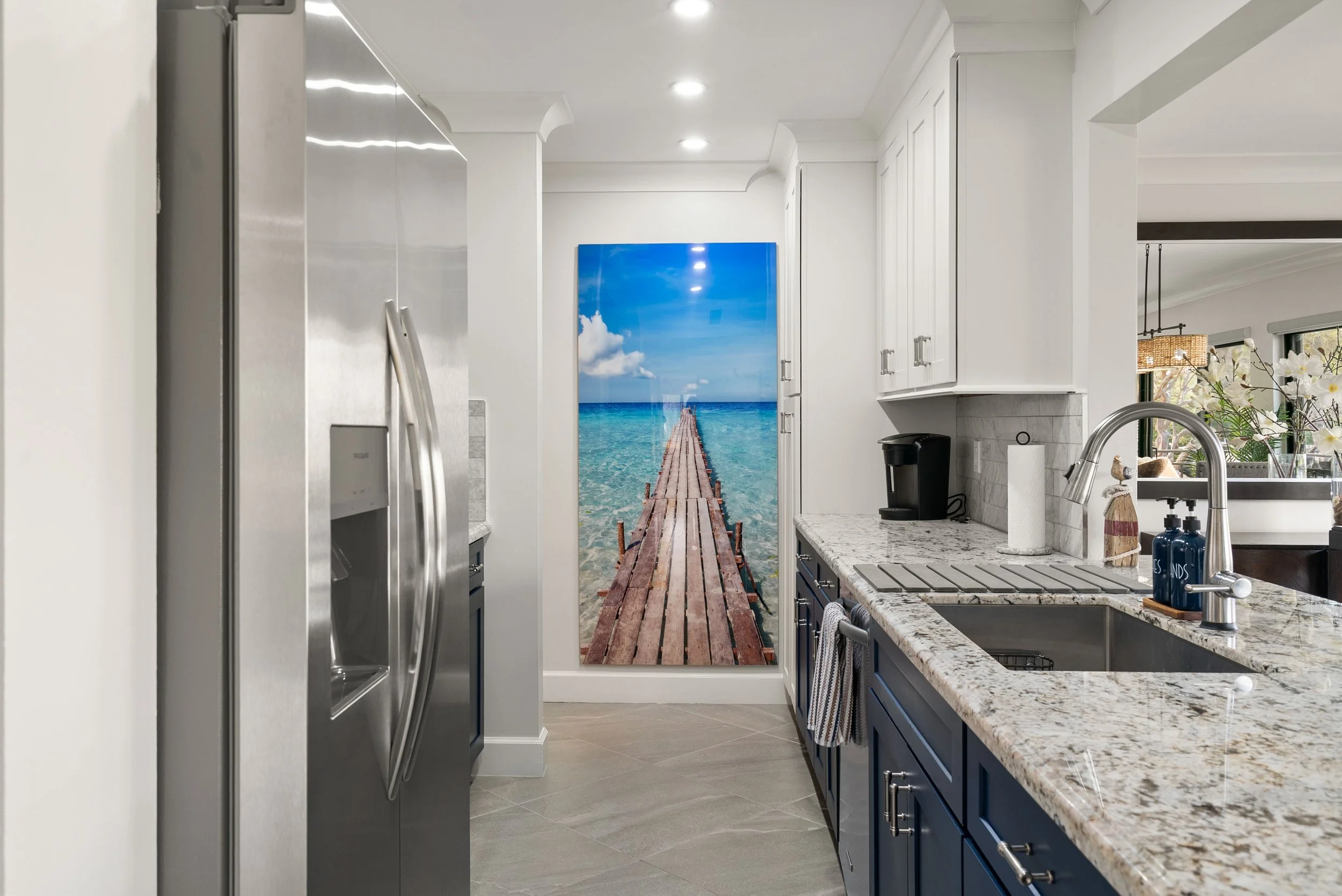 Kitchen with white and navy cabinets, granite countertops, stainless steel appliances, and a wall mural of a pier over the ocean.