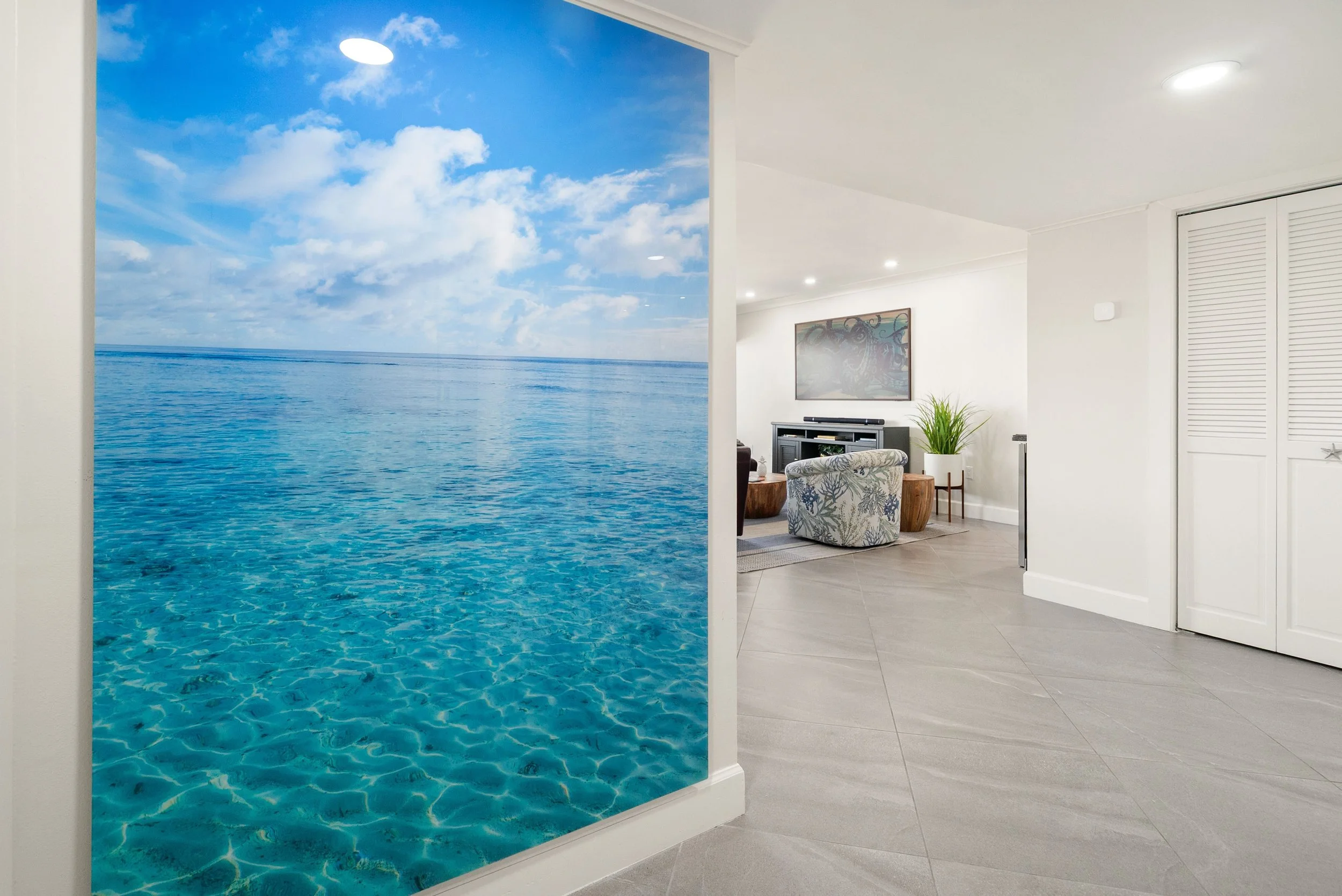 A wallpaper depicts a serene ocean scene with blue water and a partly cloudy sky on a wall in a modern living room.