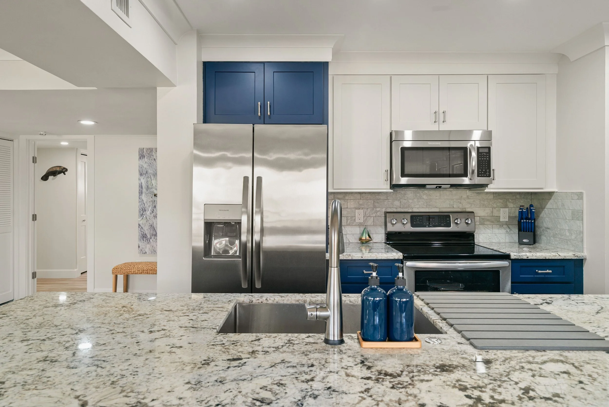 Kitchen with grey granite countertop, stainless steel refrigerator, microwave, stove, and white cabinetry with blue accents.