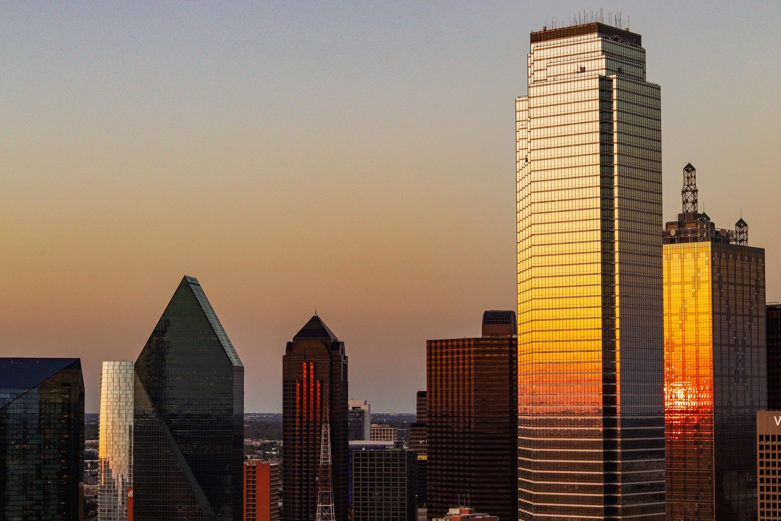 Sunset over downtown Dallas, Texas with skyscrapers reflecting the orange glow of the setting sun.