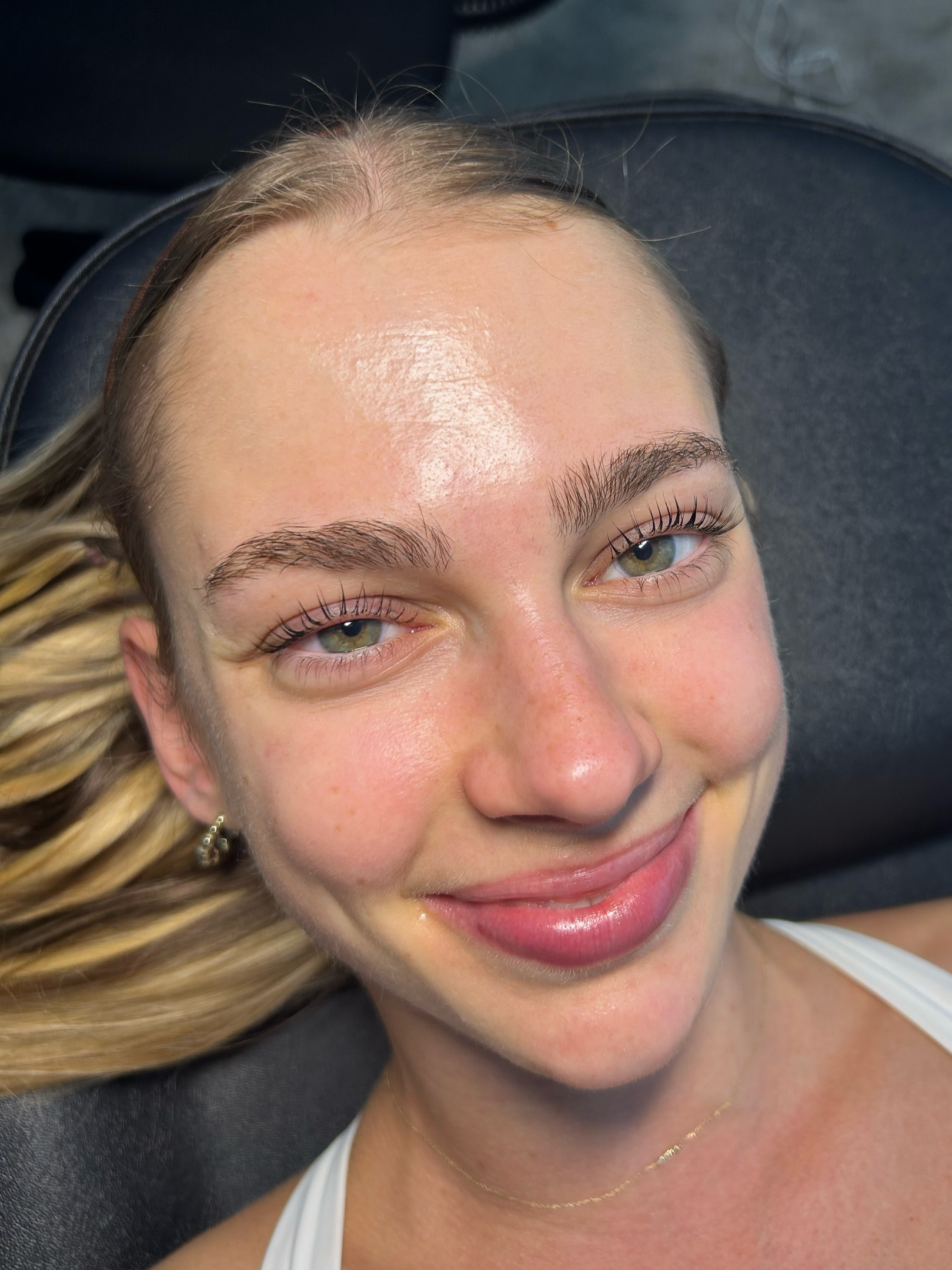 Close-up of a young woman with blonde hair, smiling, and lying down on a black surface.