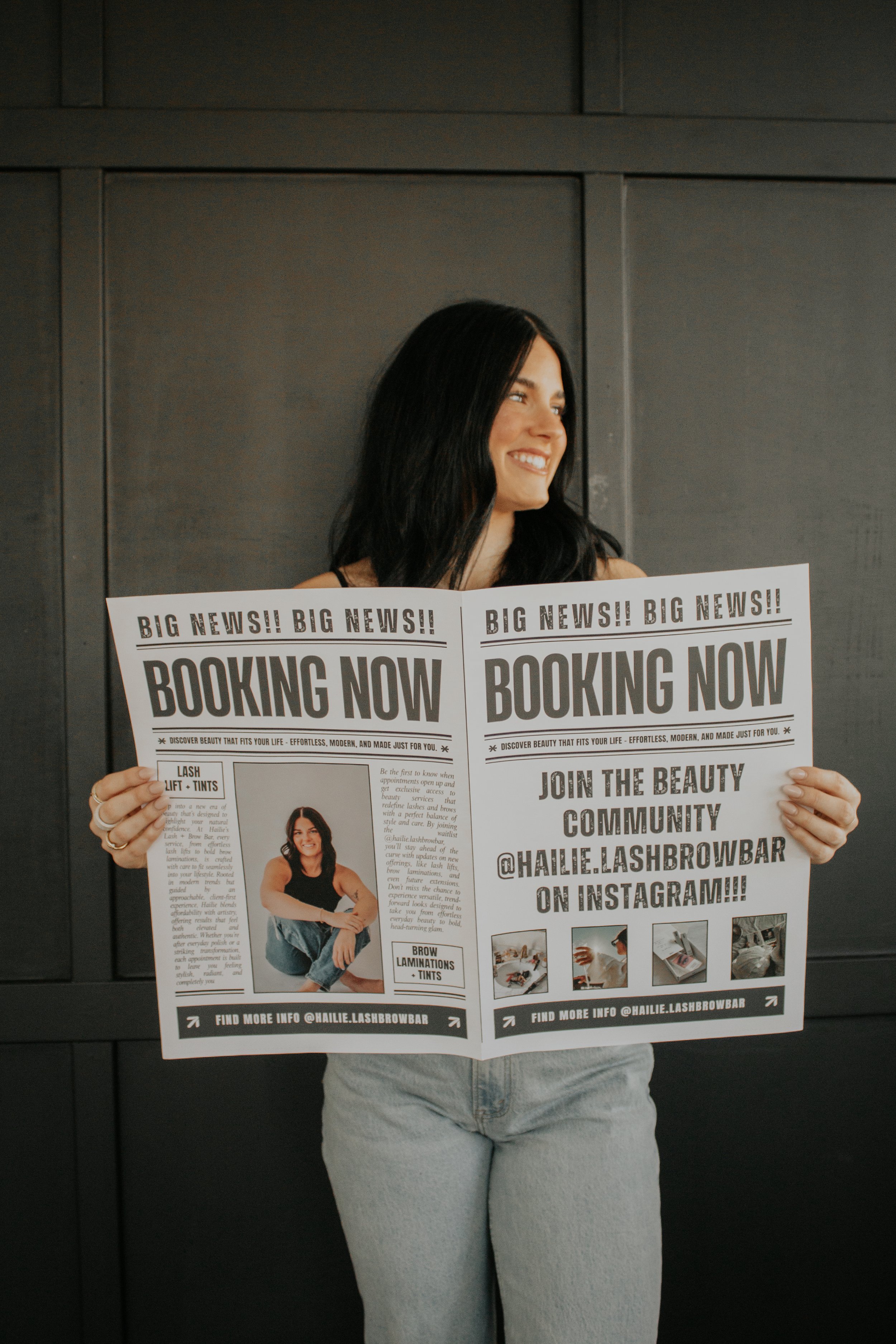 Woman with black hair holding two promotional flyers for a beauty service, standing against a dark wooden wall.