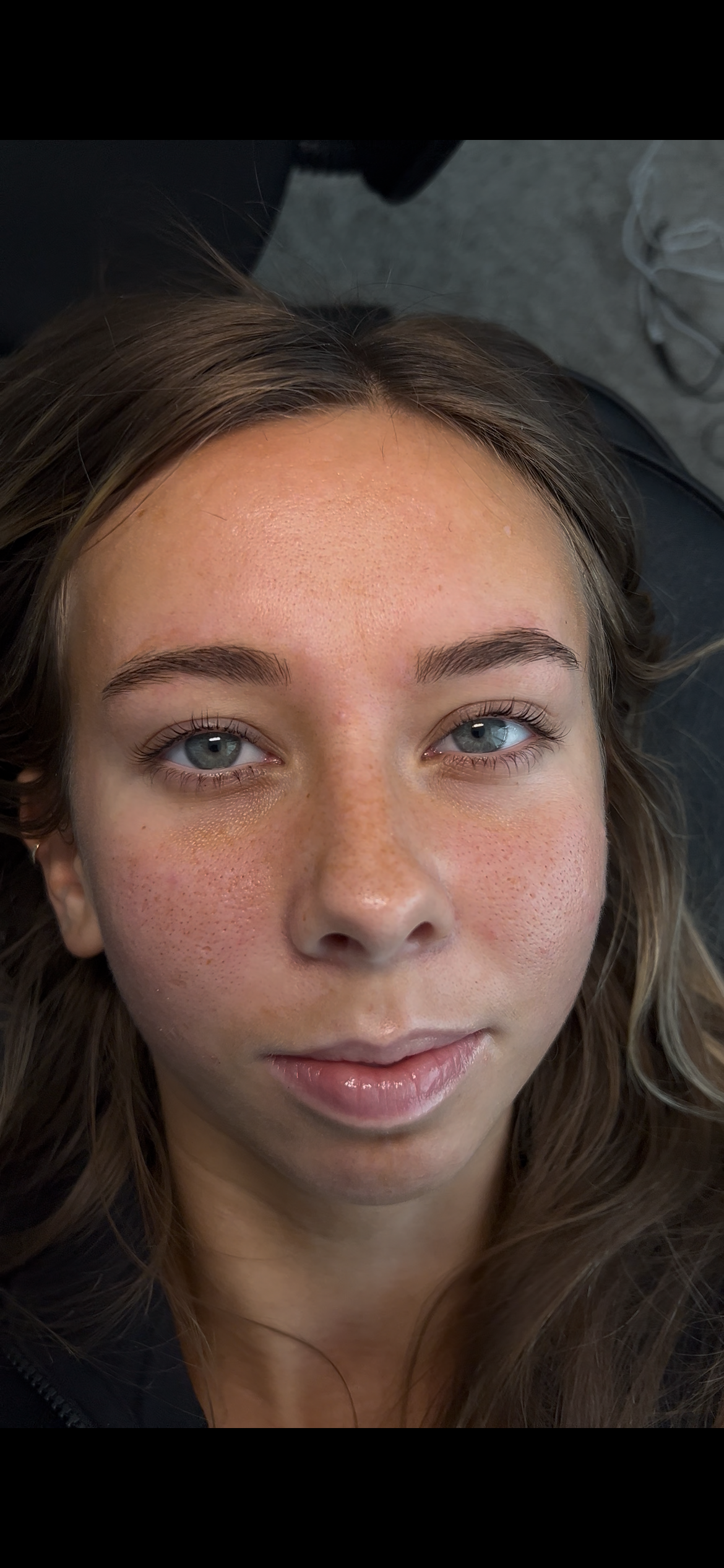 Close-up of a young woman with blue eyes and light brown hair, lying down and looking directly at the camera.