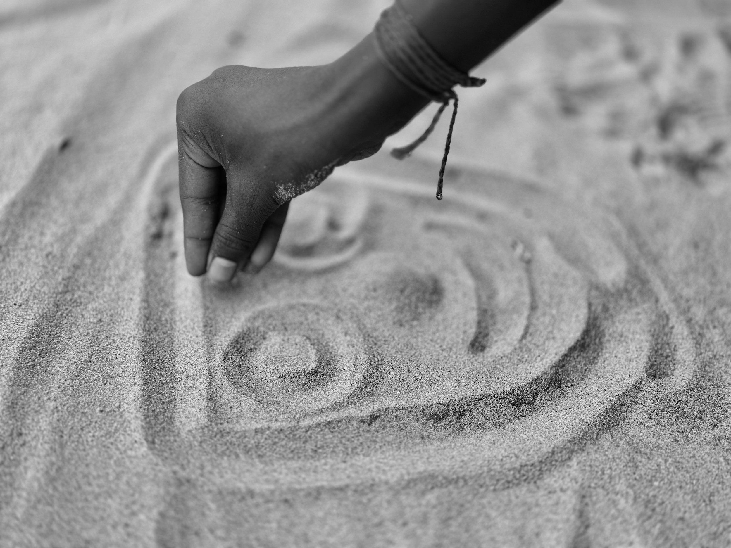 A hand with sand on fingers reaching down toward the sandy ground.
