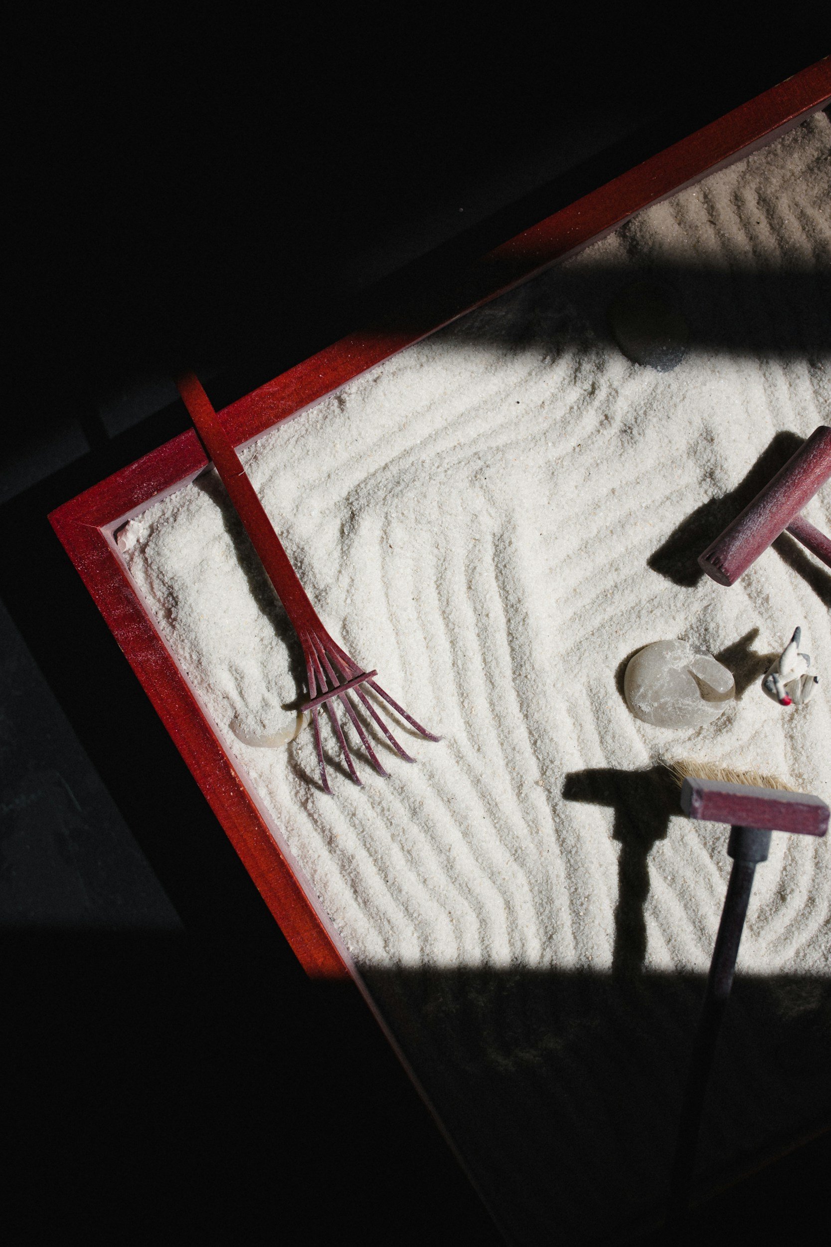 A sandbox filled with white sand, containing a red rake, a white shovel, a small plastic container, and a toy truck.