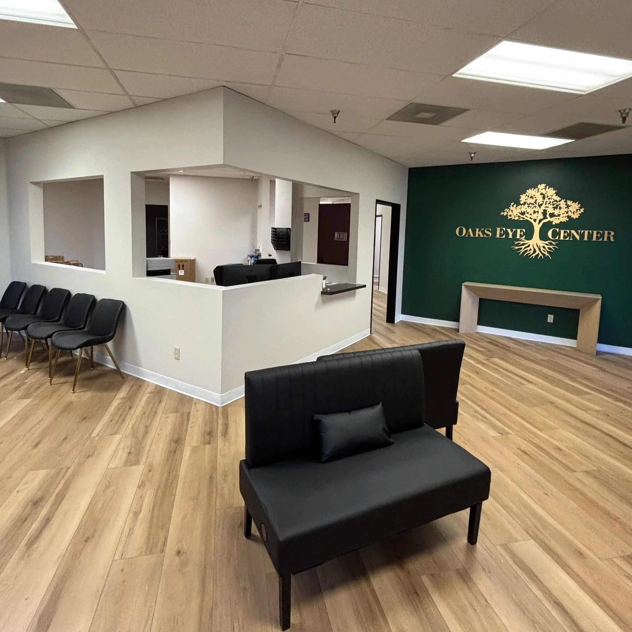 View of the waiting area at Oaks Eye Center with black chairs and a green wall with the center’s logo featuring a tree.
