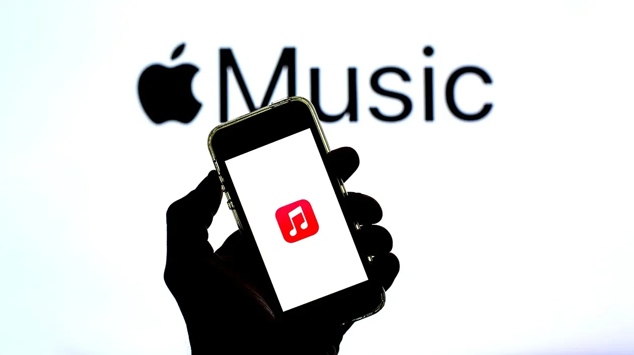 A hand holding a smartphone with a music app icon on the screen, with an Apple Music logo and the word 'Music' in the background.