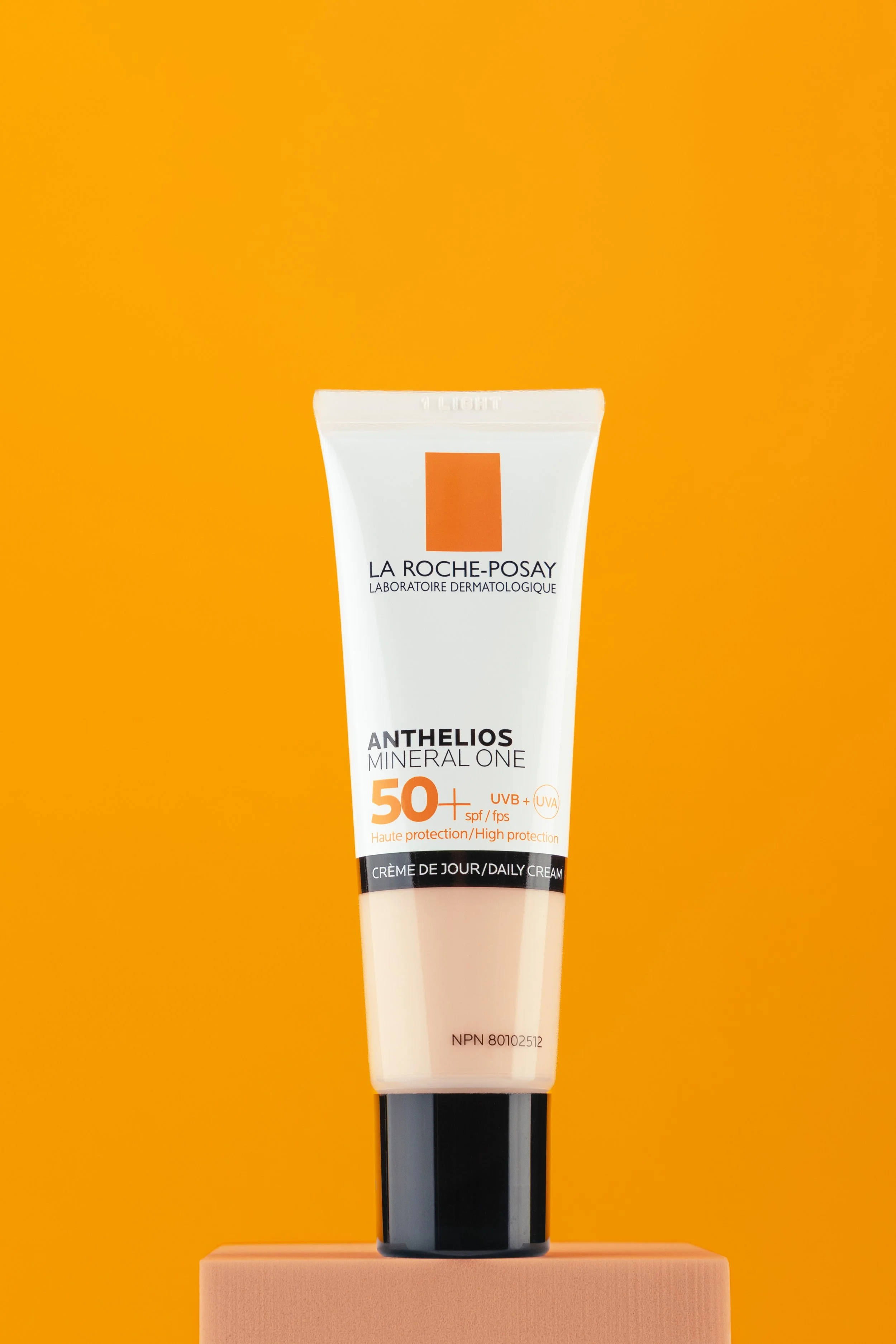 A tube of La Roche-Posay Anthelios Mineral One Daily Cream with SPF 50+ standing vertically on a pink platform against a yellow background.