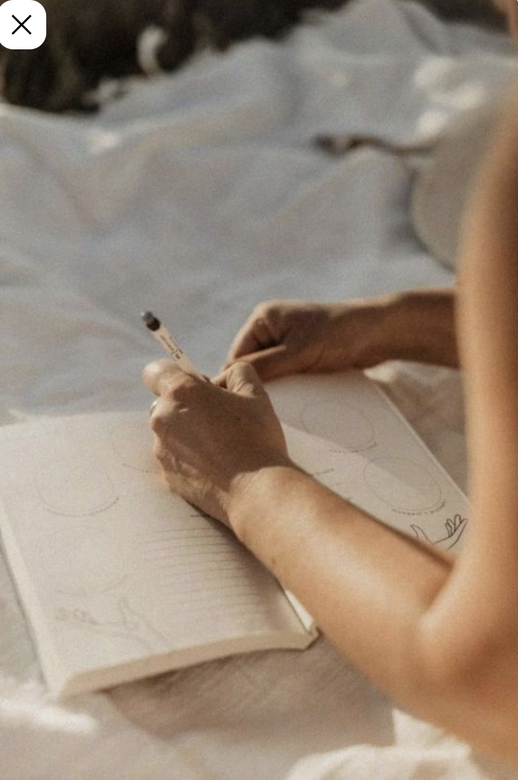 A person writing in a notebook with a pen, with a coffee cup nearby on a light-colored surface.