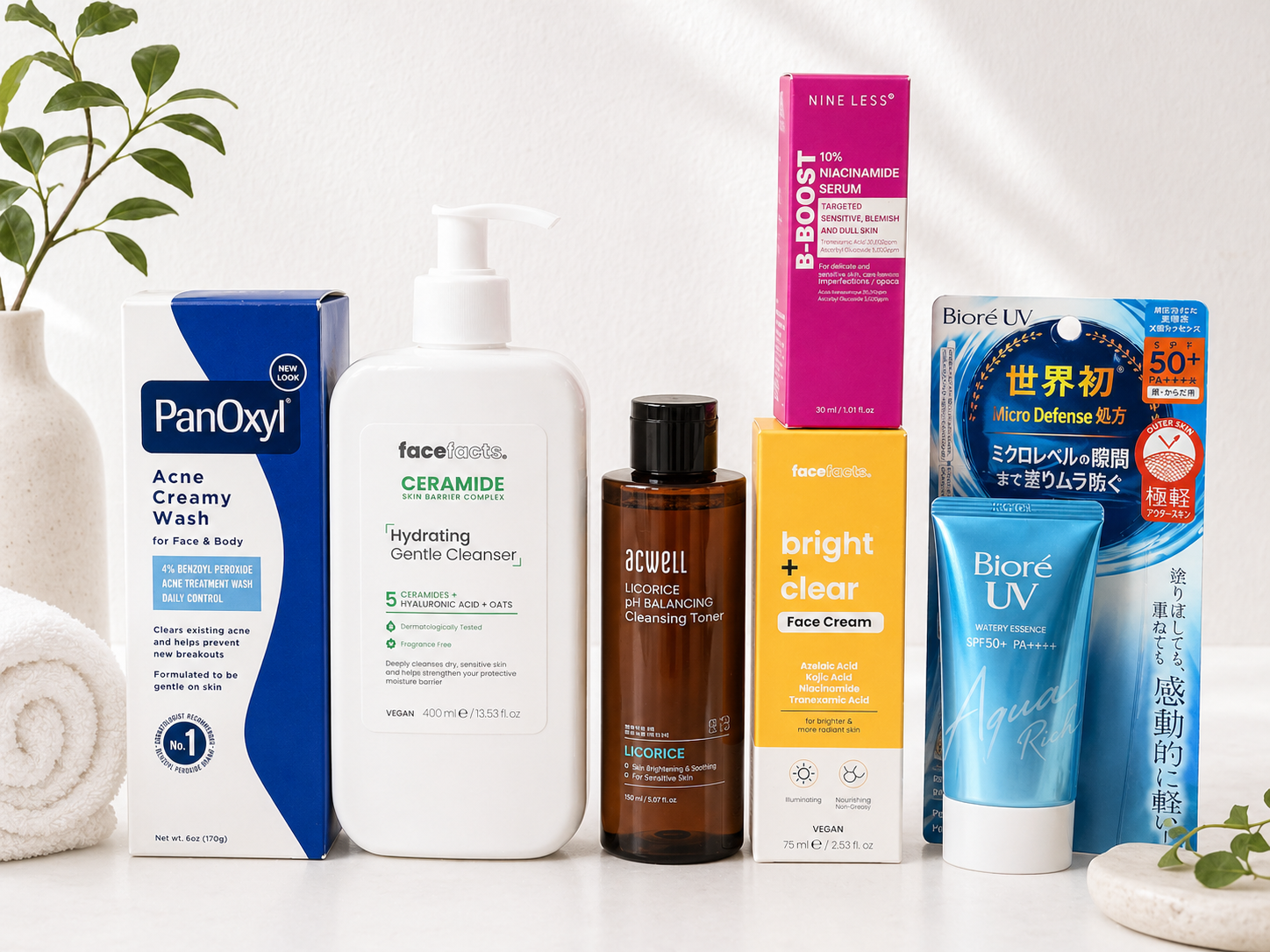 A collection of skincare and beauty products including PanOxyl Acne Creamy Wash, Face Facts Ceramide Hydrating Gentle Cleanser, Acwell Licorice pH Balancing Cleansing Toner, Face Facts Bright and Clear Face Cream, a pink box of Nine Less B-Boost, Biore UV Micro Defense, a blue Biore UV Watery Essence, and a blue sheet mask on a white surface with a small potted plant on the left.