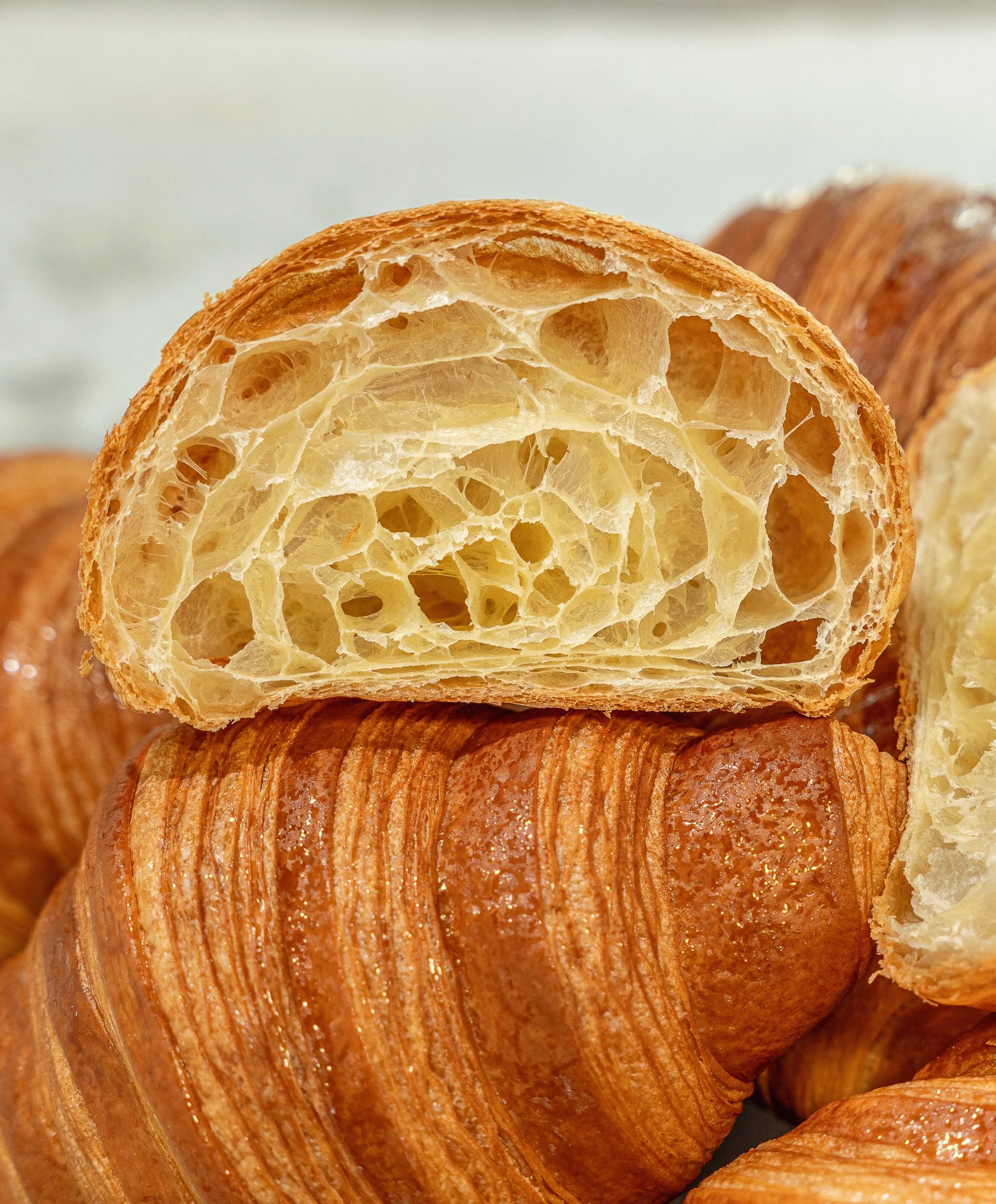 Close-up of a croissant, showing its flaky, golden-brown exterior and airy interior with many holes and layers.