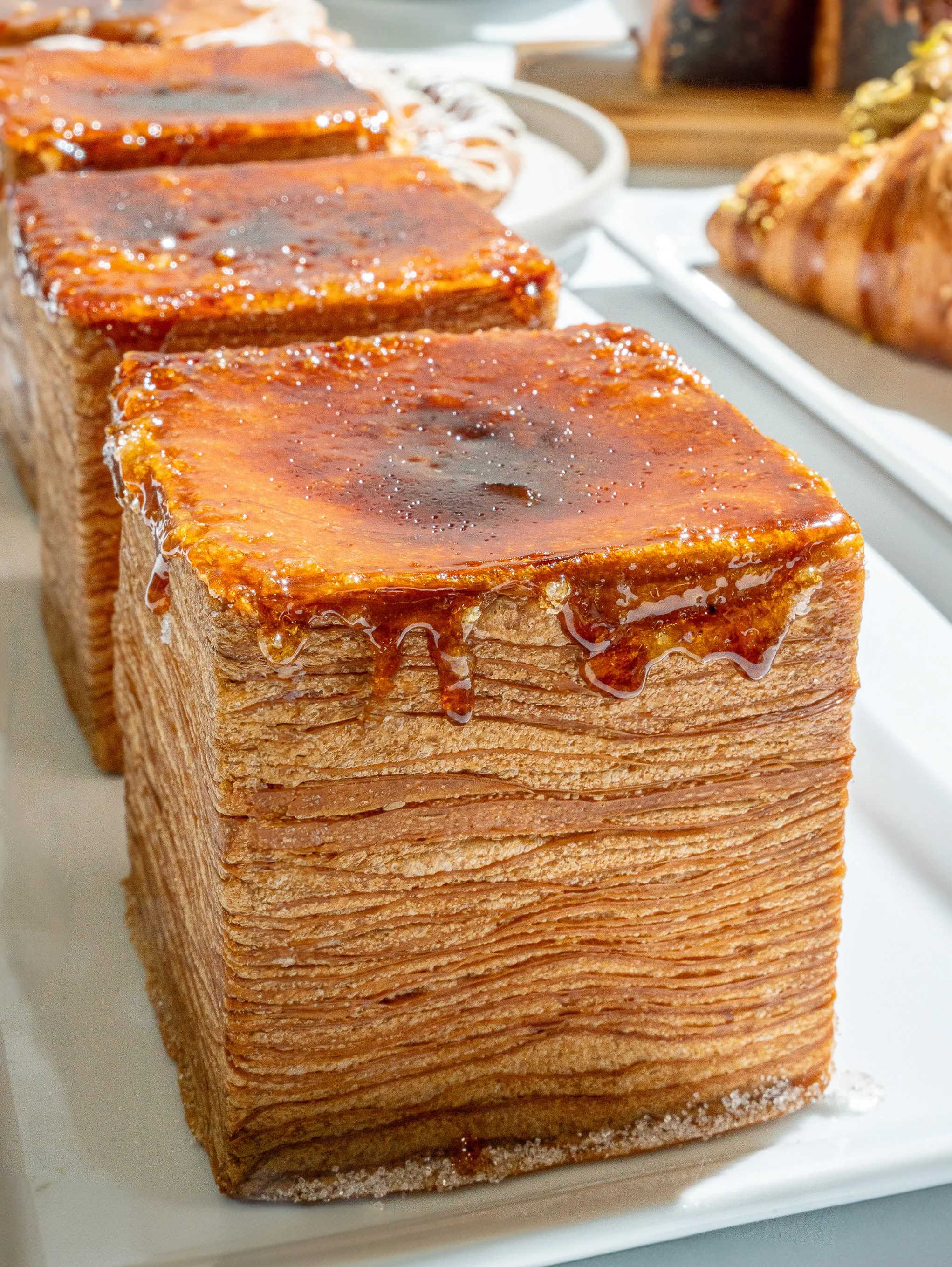 Close-up of a layered caramel cake with glossy caramel glaze on top, with a caramel swirl pattern on a white platter.