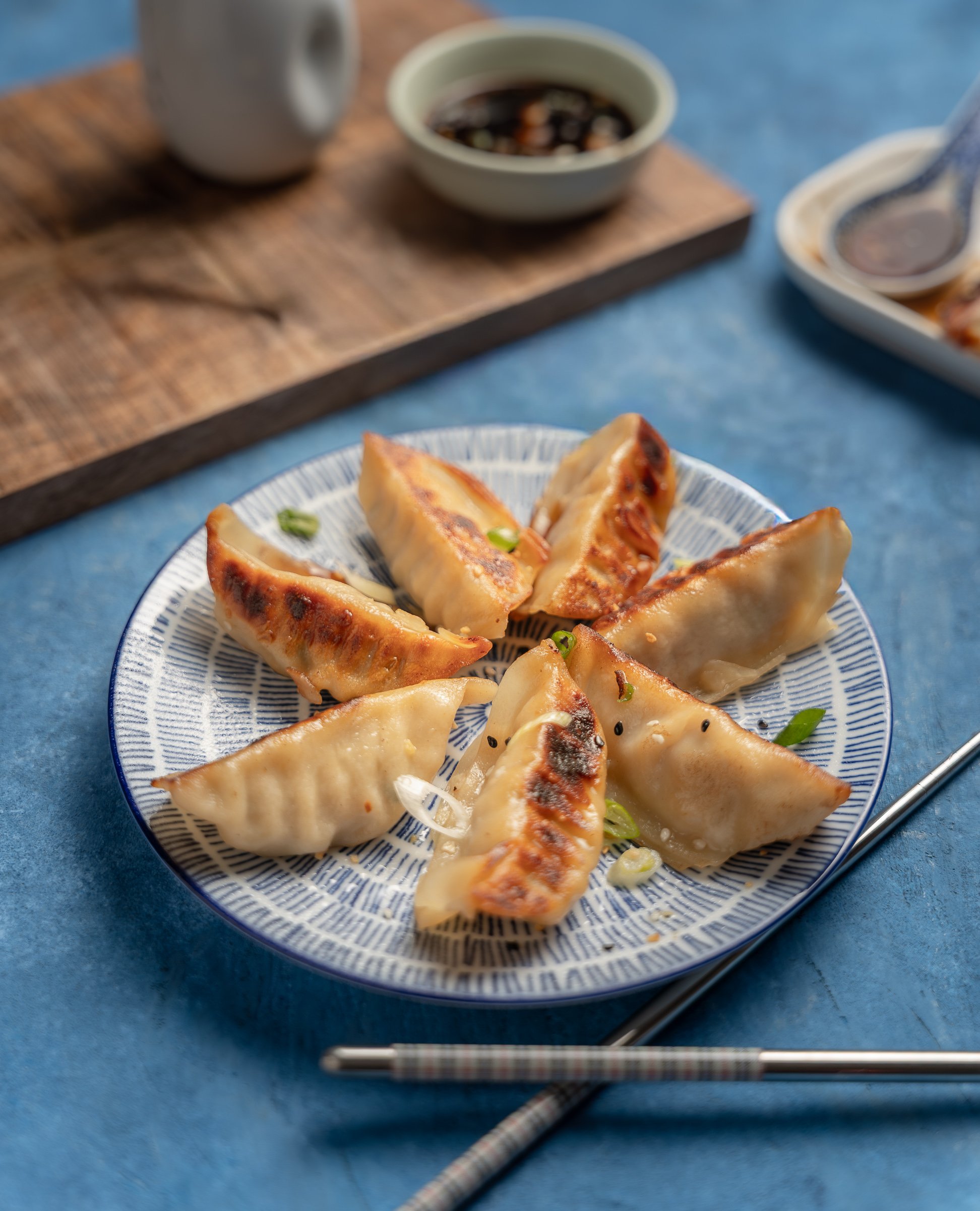 Artisanal Gyoza | Asian Fusion Food Styling
Professional food photography of pan-fried dumplings (gyoza) served on a patterned blue ceramic plate. This high-contrast shot features expert lighting on the crispy golden textures, set against a vibrant b
