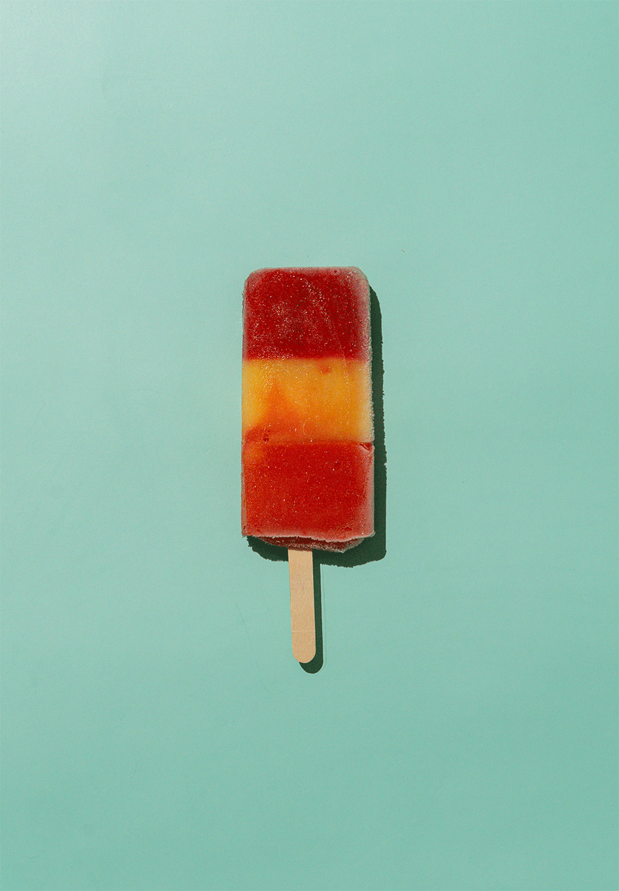 Colorful frozen popsicle with red, orange, and yellow layers on a light blue background.