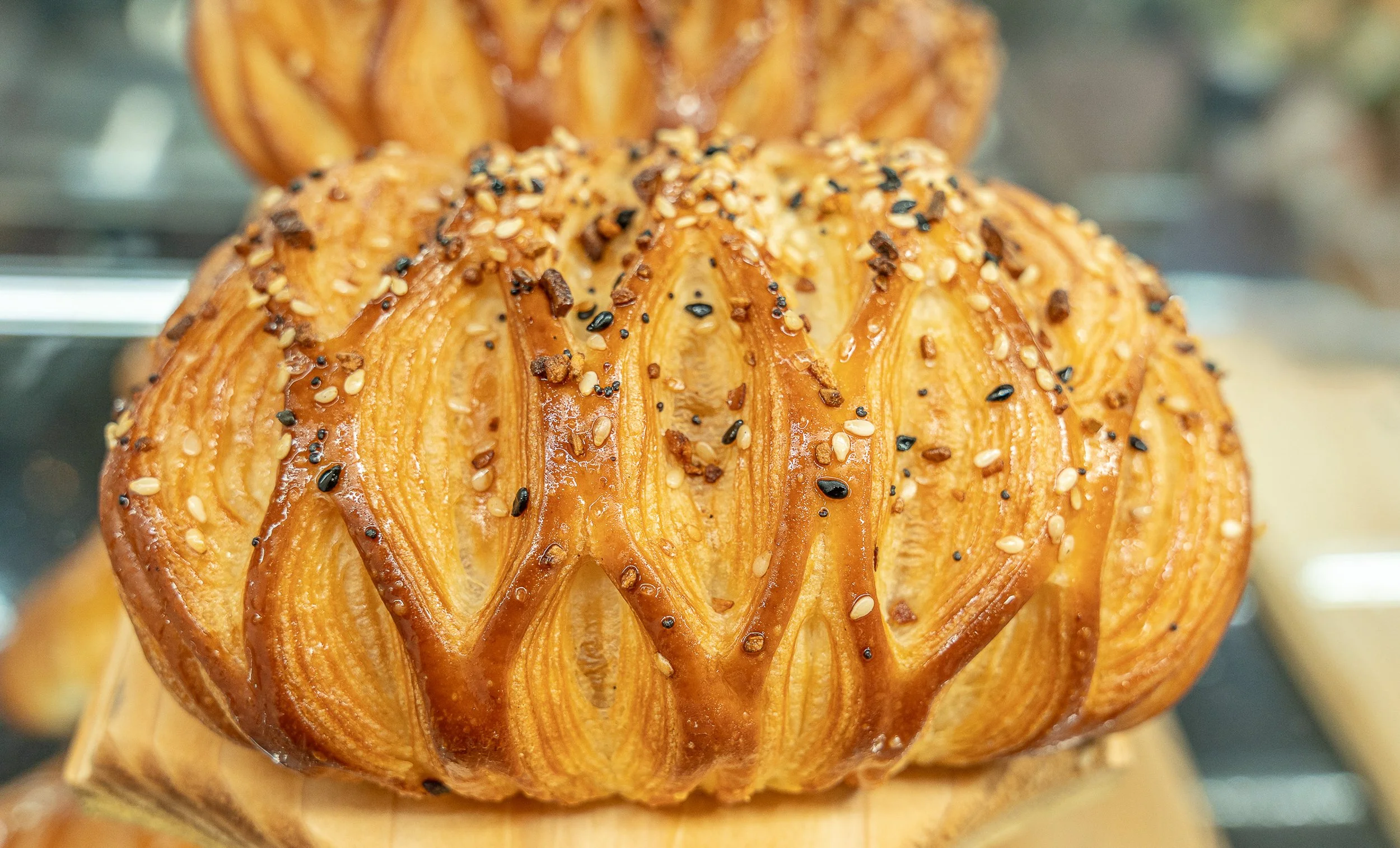 Close-up of a baked, spiral-shaped pastry with a golden-brown crust, topped with sesame seeds and black seeds.
