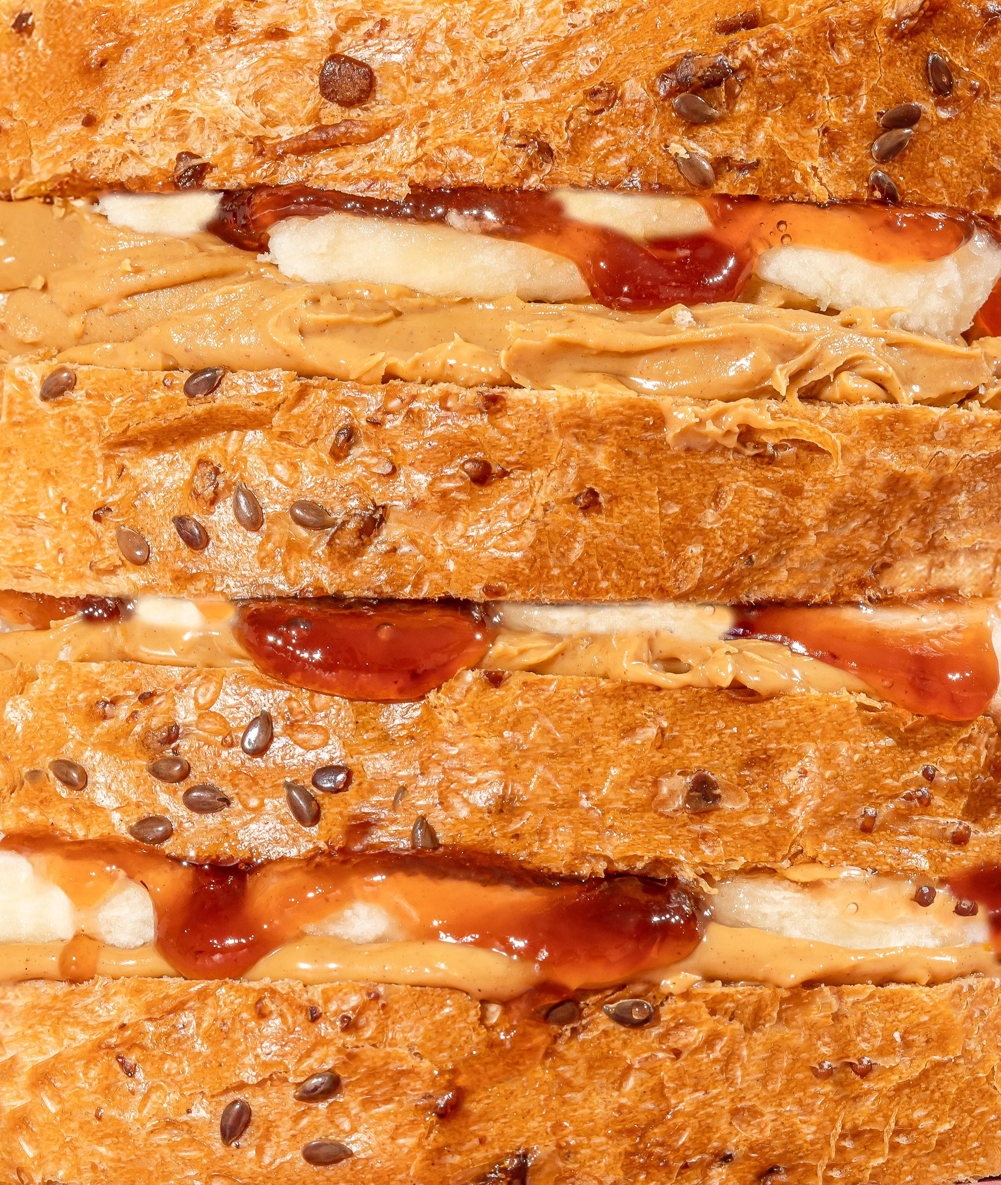 Close-up of a sandwich with toasted bread, peanut butter, jelly, and sprinkled flax seeds.