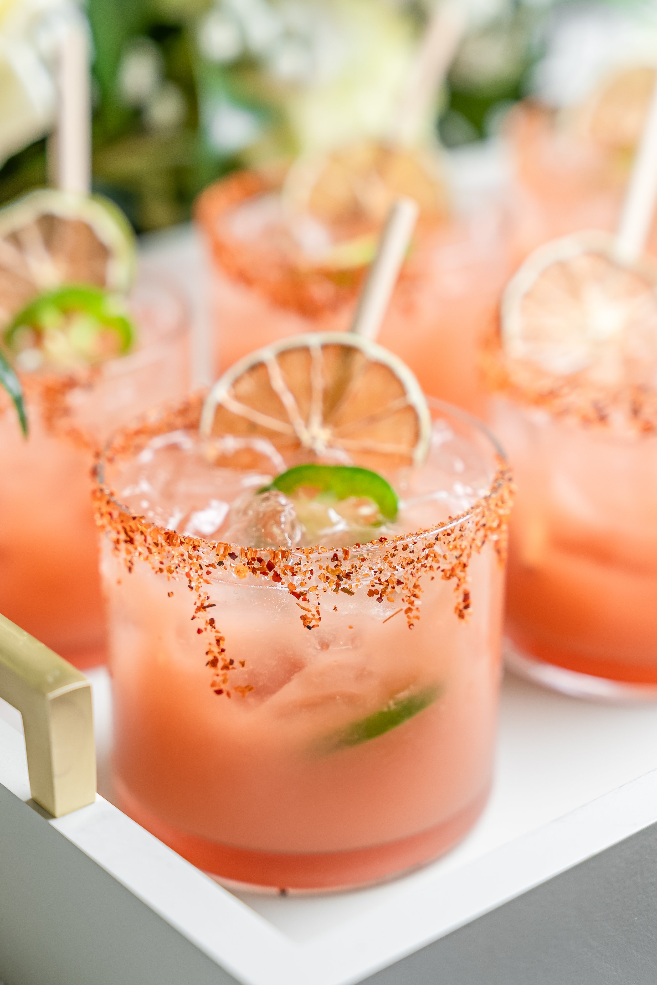 Close-up of pink margarita cocktails garnished with lime slices and salted rims, served on a white tray.