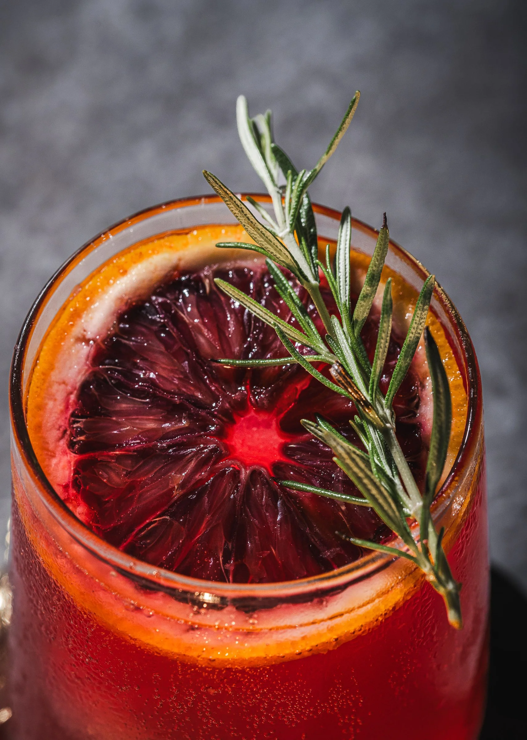 Blood orange + rosemaryCommercial cocktail photography in Miami featuring a blood orange drink with rosemary garnish, highlighting texture, freshness, and natural styling for restaurant branding.
