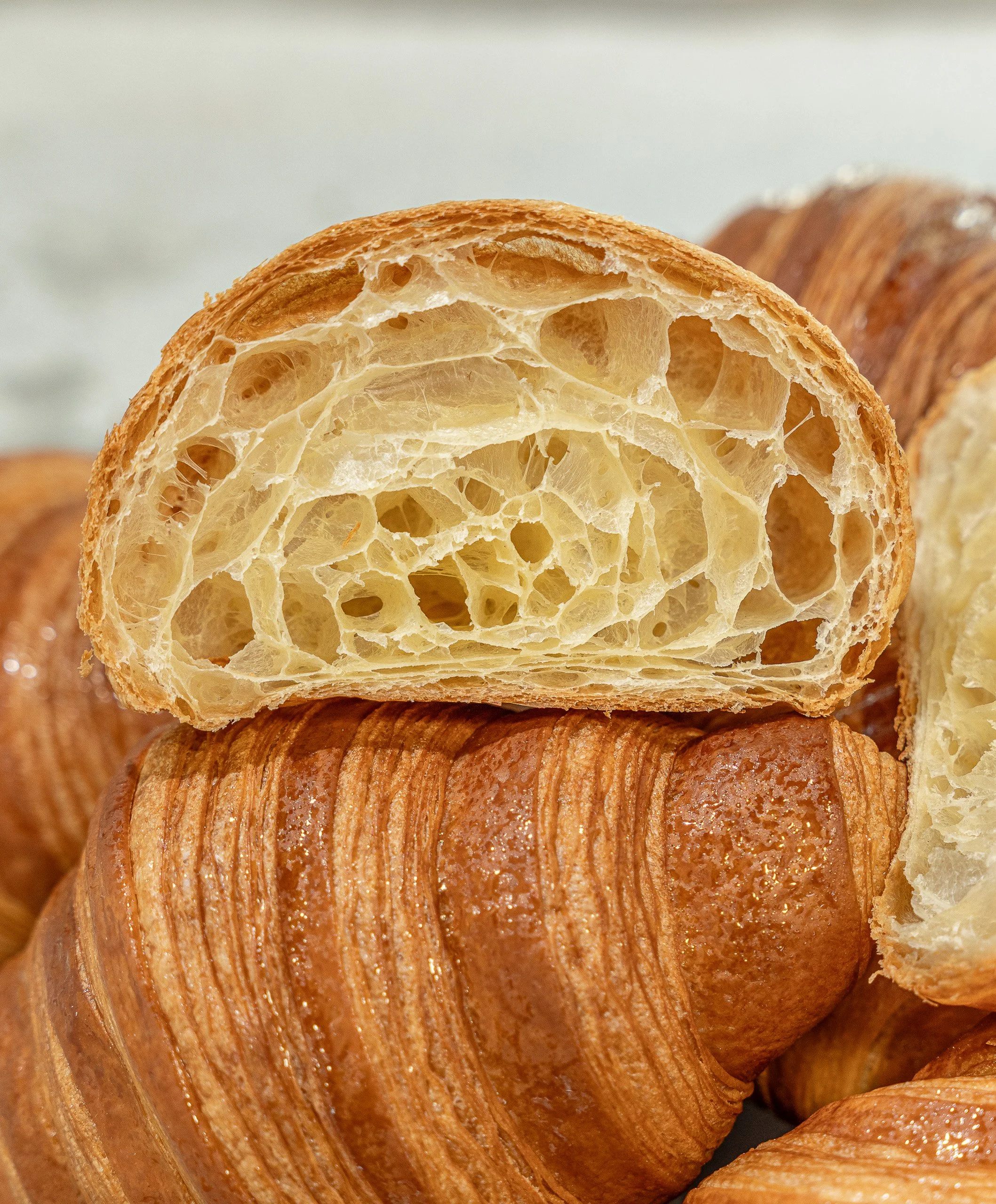 Close-up of a croissant, showing its flaky, golden-brown exterior and airy interior with many holes and layers.
