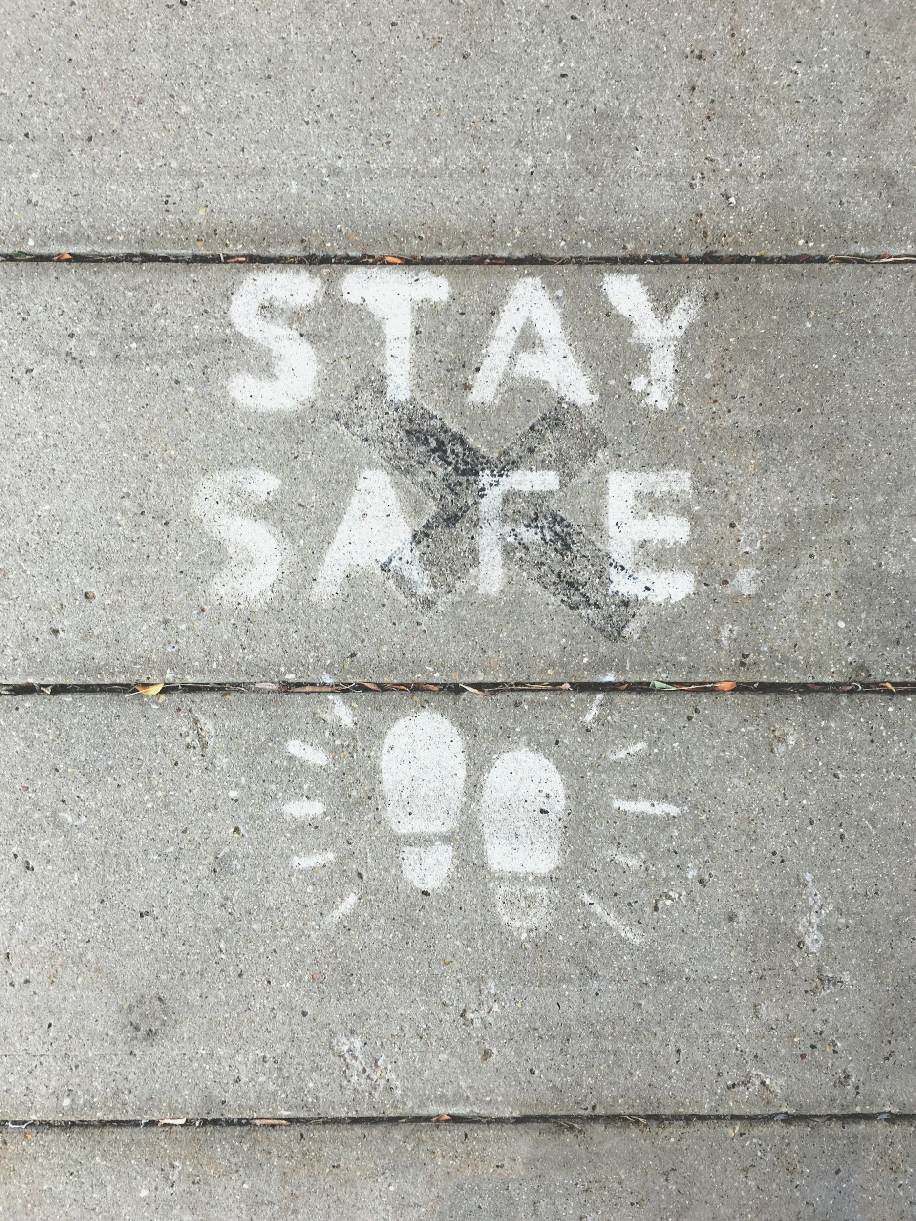 Concrete sidewalk with a painted message that reads 'STAY SAFE' and a pair of footprints with lines radiating from them.