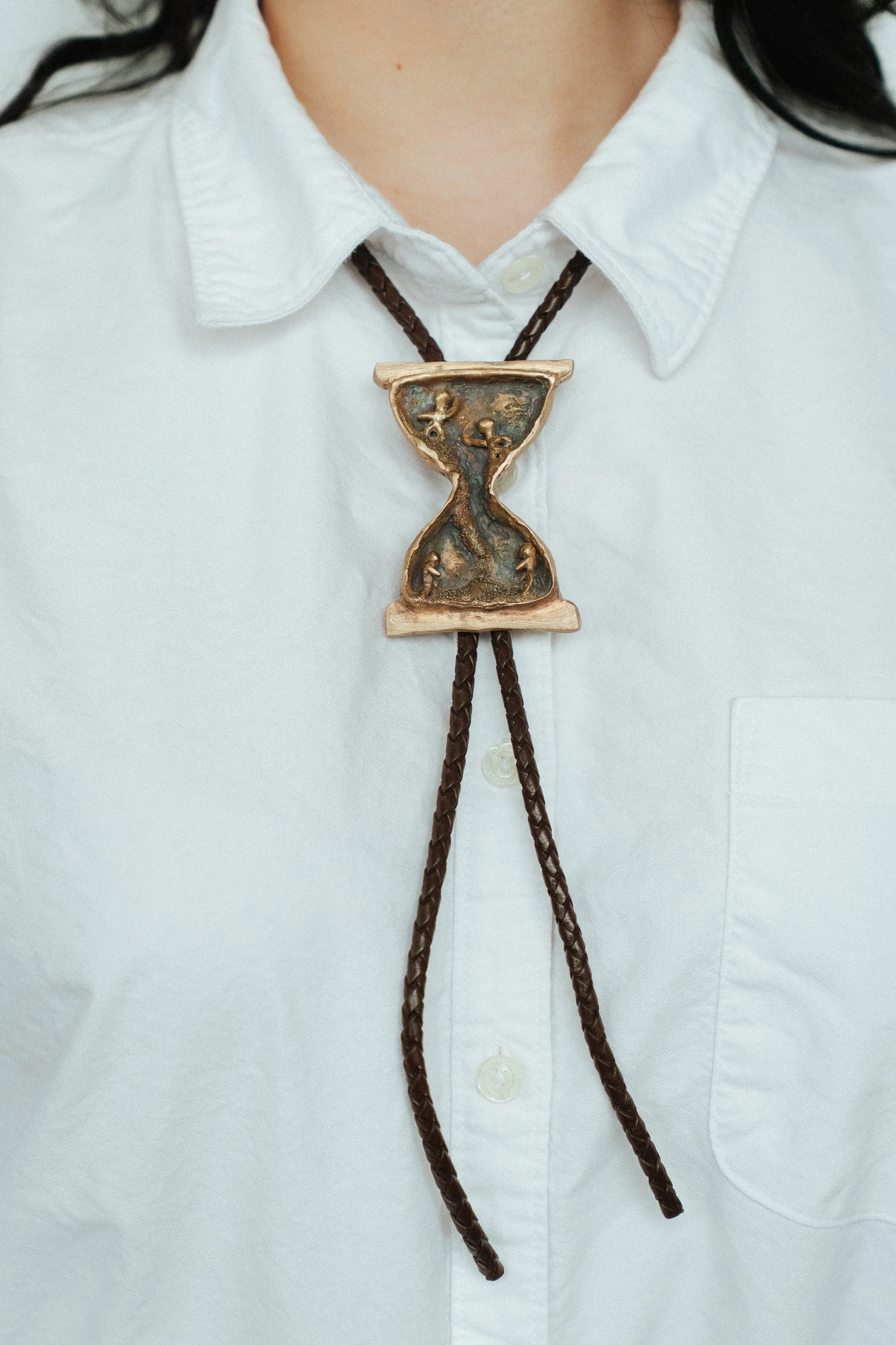 This bolo tie shows human figures inside an hour glass. This figures at the top are young and joyful, while the ones on the bottom are shrugging as they feel their time running out.