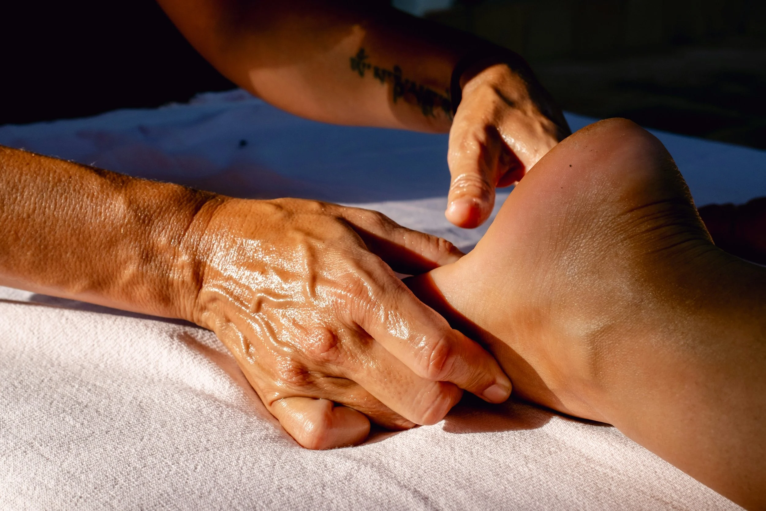 Close-up of a massage therapist's hands massaging a person's foot on a white towel.