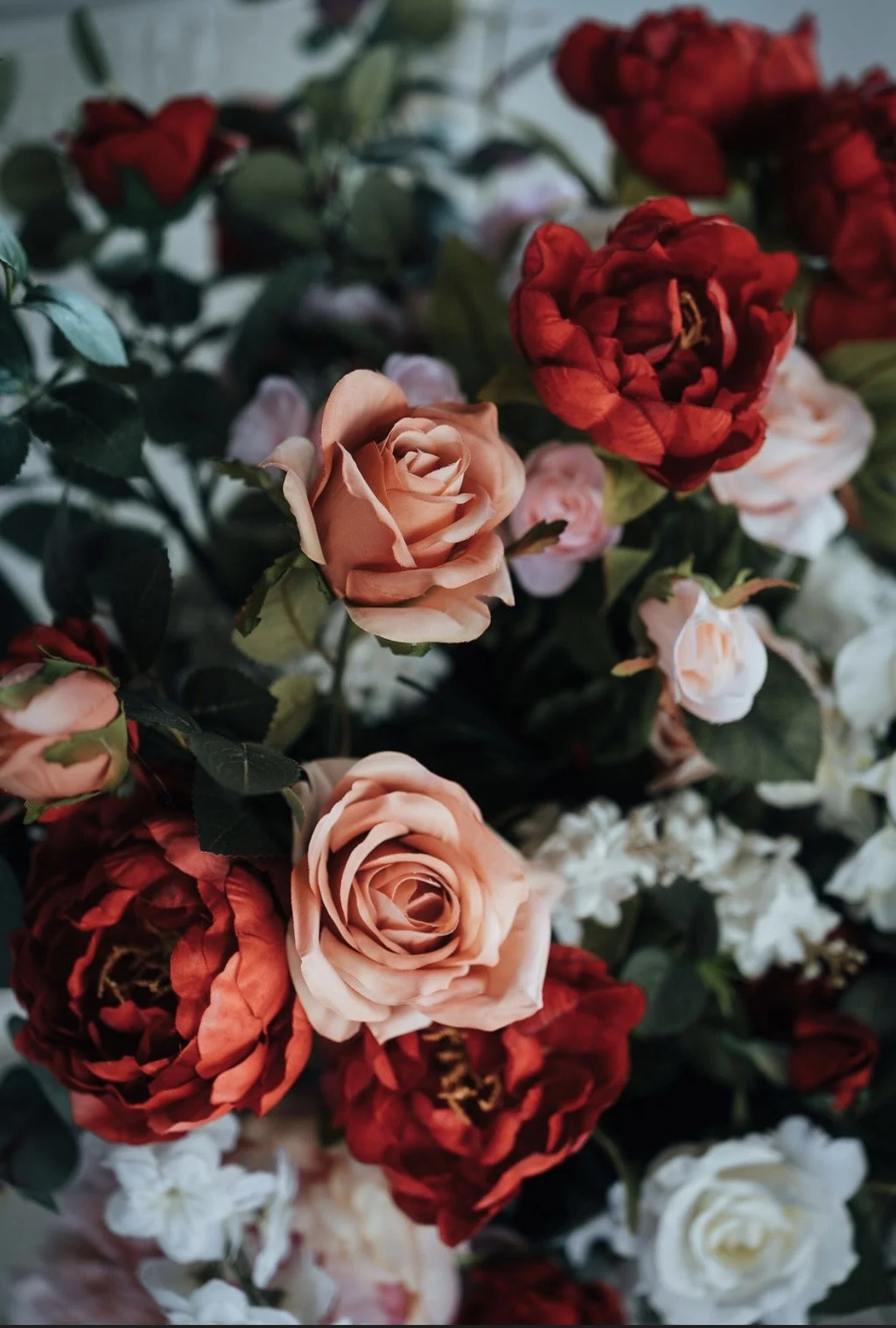 A close-up of a mixed bouquet of roses in shades of peach, red, and white with green leaves.