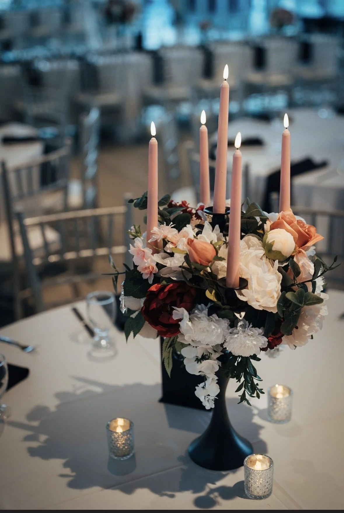 A floral centerpiece with pink candles on a dinner table at an elegant event, decorated with white and red flowers and surrounded by small lit candles.